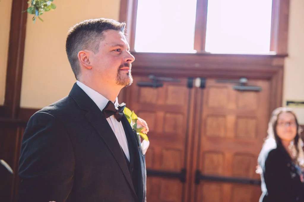 A groom seeing his bride for the first time as she walks down the aisle during their wedding ceremony at Searles Chapel in Windham, NH. Wedding photography by Mike Indi.