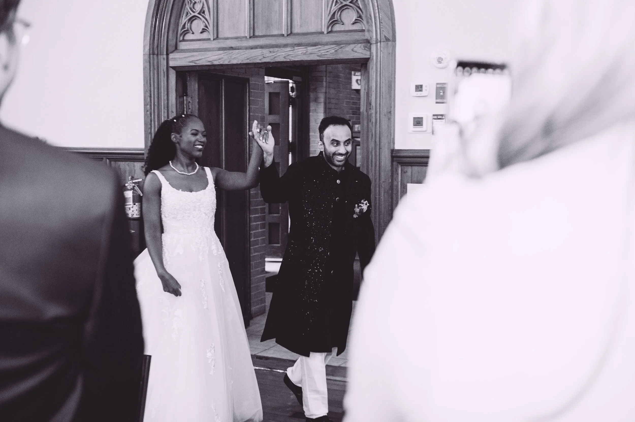 A bride and groom entering their wedding reception smiling and holding their hands in the air as they receive a thunderous applause during their wedding reception at Searles Chapel in Windham, NH. Wedding photography by Mike Indi.