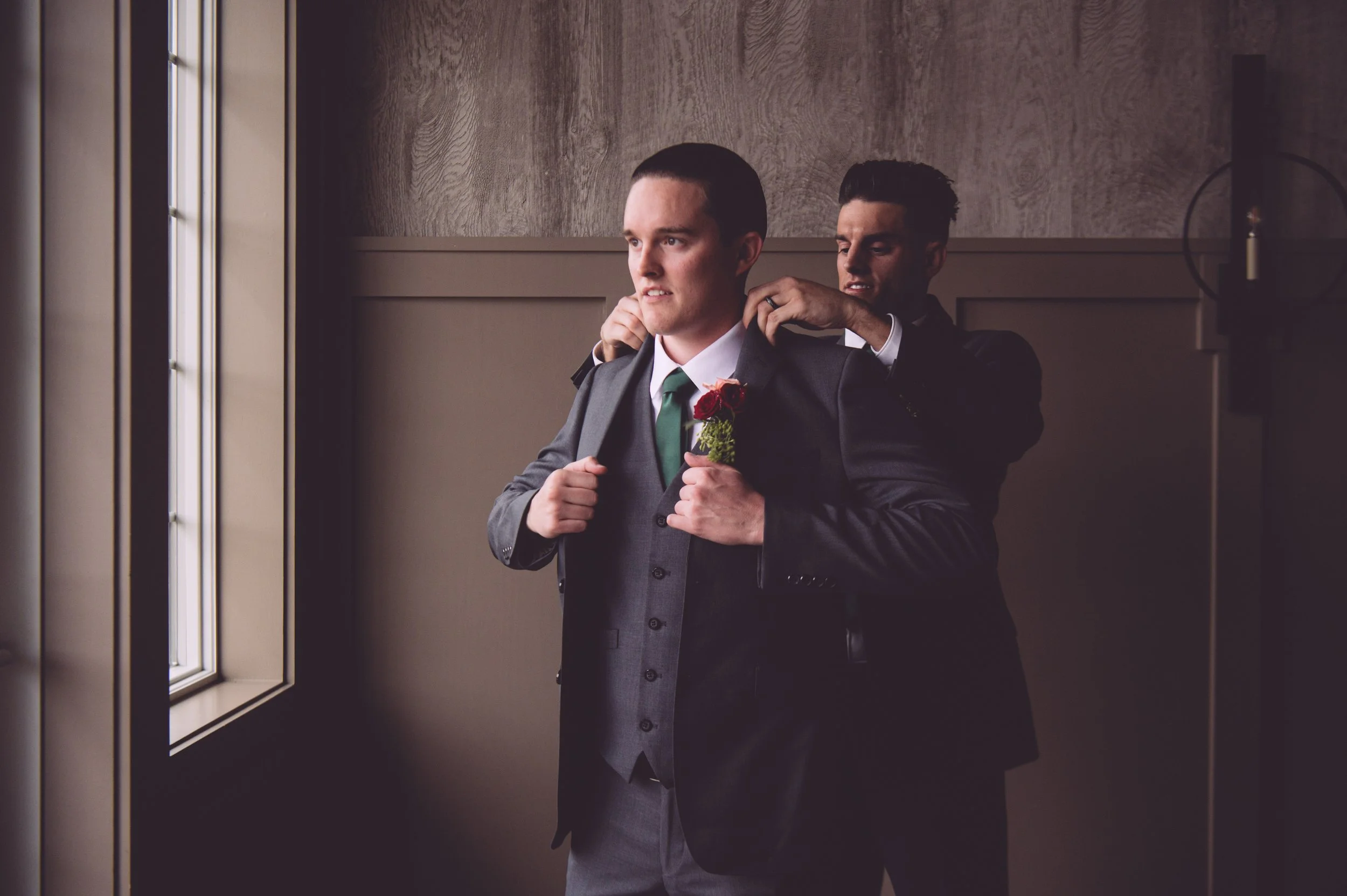A groom putting on his suit jacket with the help of his best man before his wedding at LaBelle Winery in Derry, NH. Wedding photography by Mike Indi.