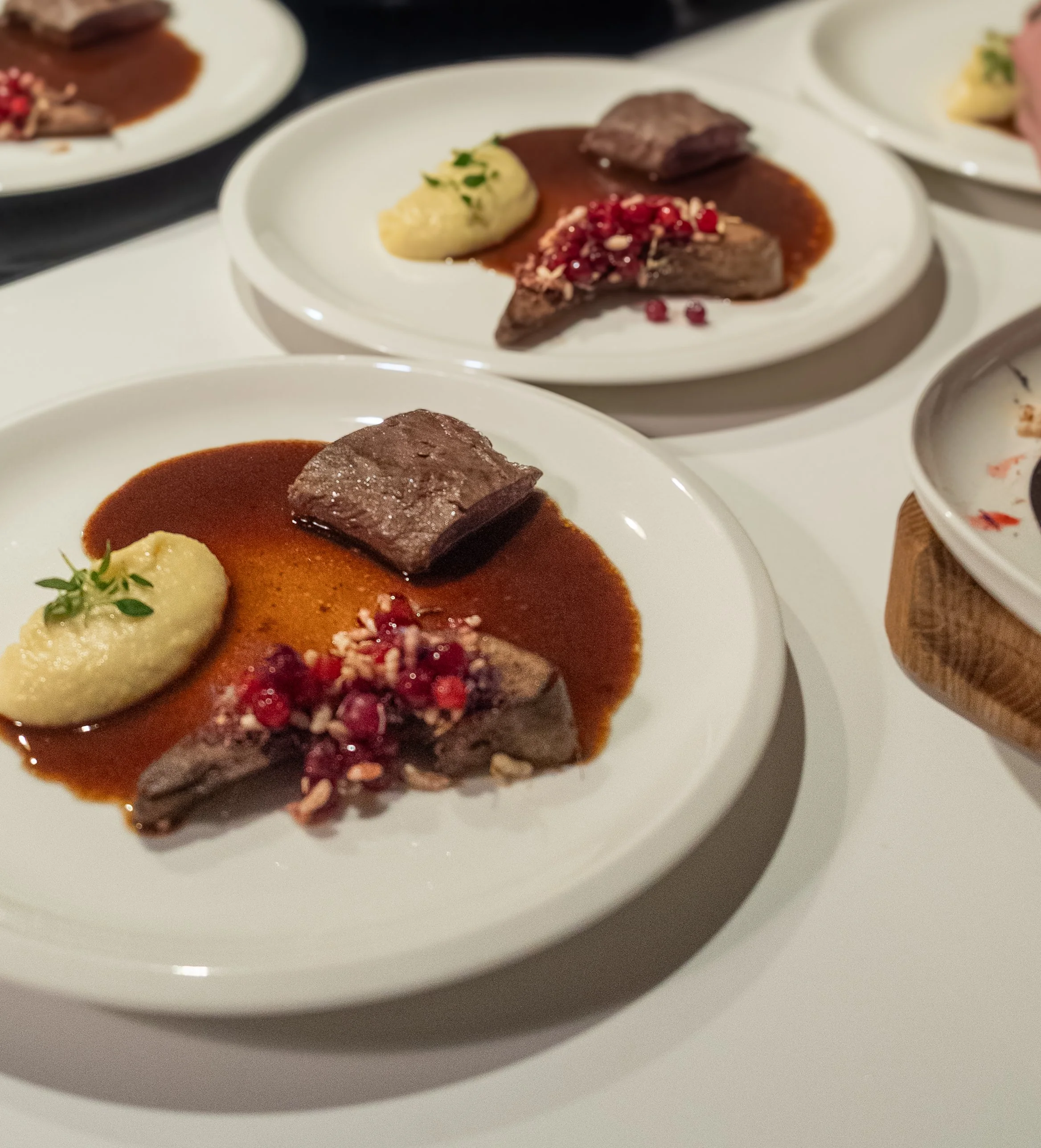 Plates with portions of beef served with sauce, mashed potatoes, and garnishes on a white table.