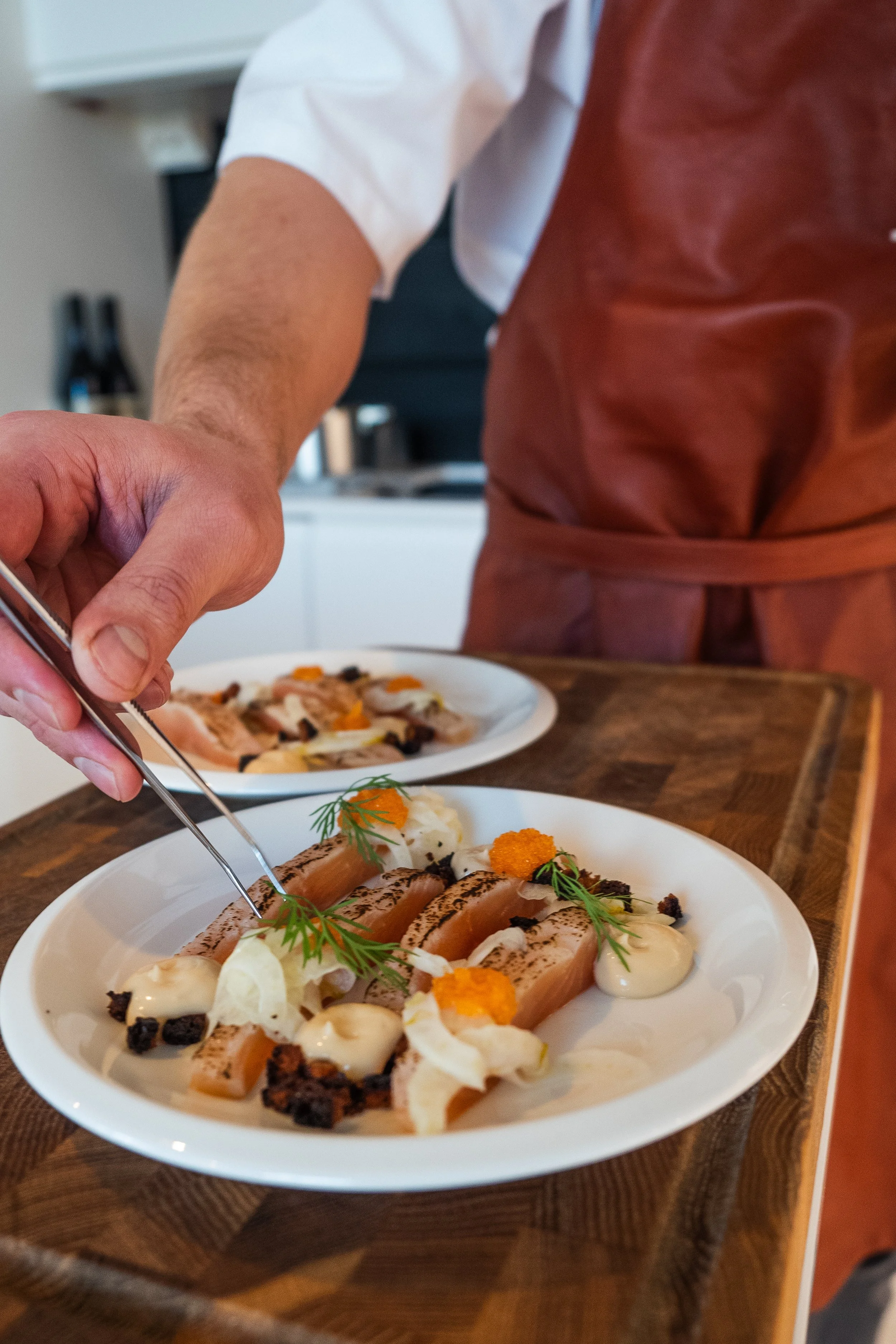 Chef garnishing a plated dish with herbs and caviar in a restaurant kitchen.