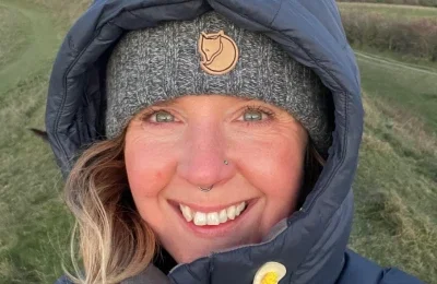 Close-up of a smiling woman wearing a gray beanie and a navy jacket outdoors.