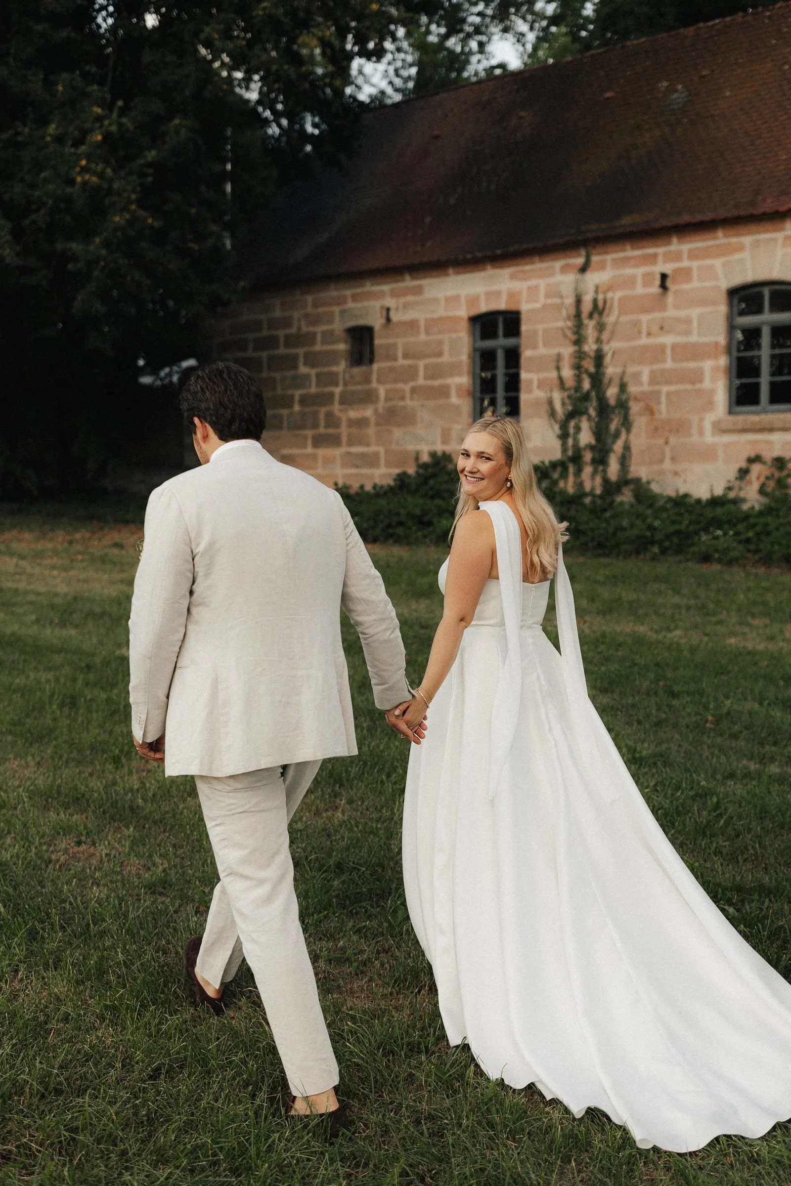 Minimalistisches Brautpaar läuft Hand in Hand vor Schloss Dürrenmungenau in einem Stilvollen Brautkleid