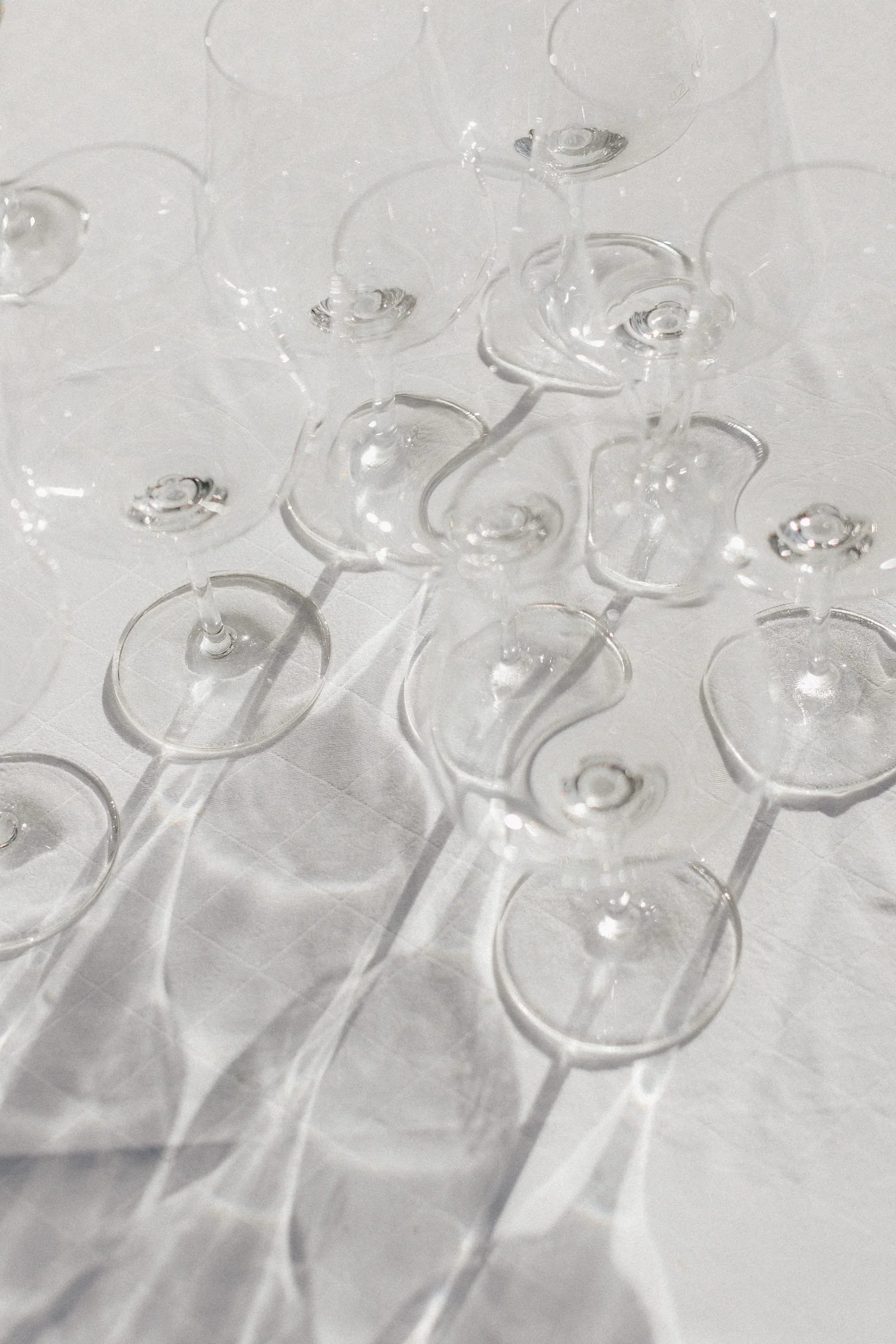 Mehrere leere Weingläser im Weingut Boudier Koeller aus transparentem Glas auf einem weißen Tisch, mit Schatten und Reflexionen.