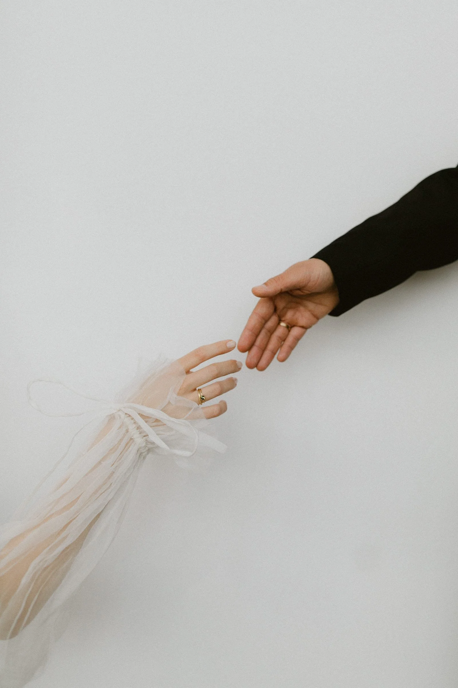 Eine Hand in einem schwarzen Ärmel reicht eine zarte, weiße Hand mit Spitze und Schleife auf dem Ärmel die Hand.