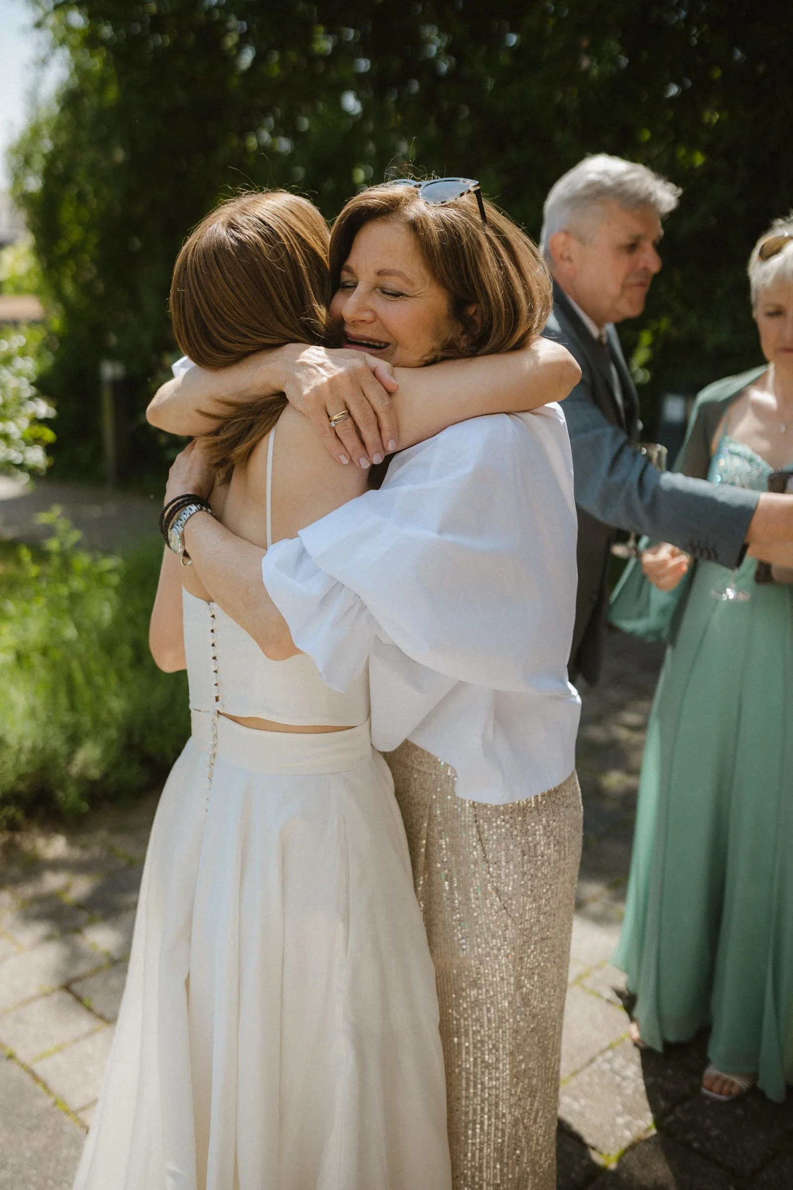 Mutter und Tochter umarmen sich vor natürlichem bewaldeten Hintergrund und lächeln berührt.