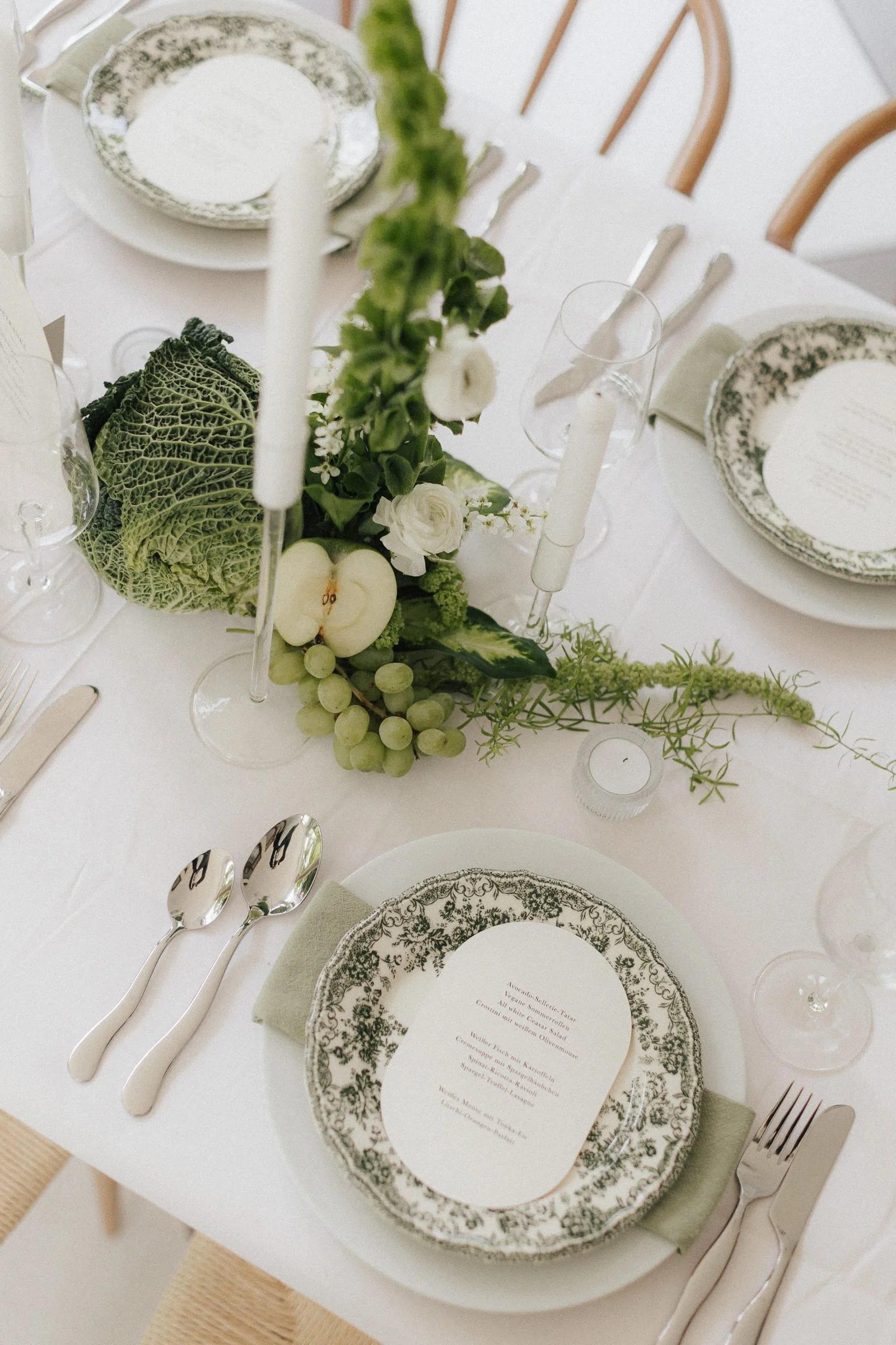 Eleganter gedeckter Esstisch mit Blumen, Kerzen und Geschirr im Greenery-Stil.