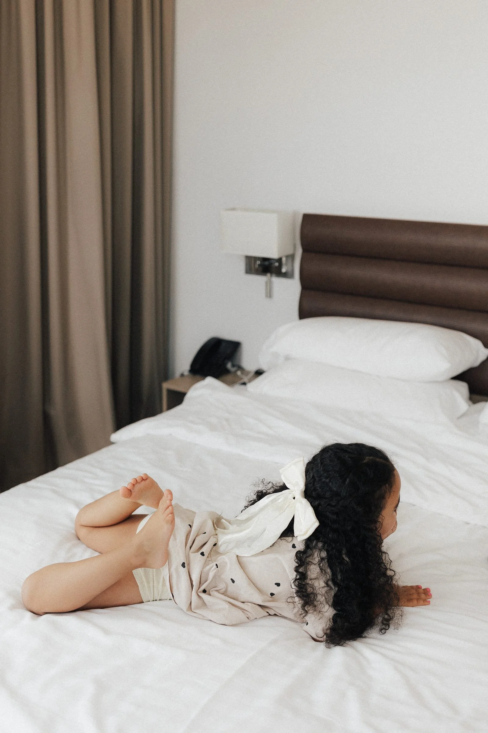 Ein Mädchen liegt auf einem Hotelbett auf dem Bauch mit hochgezogenen Beinen.