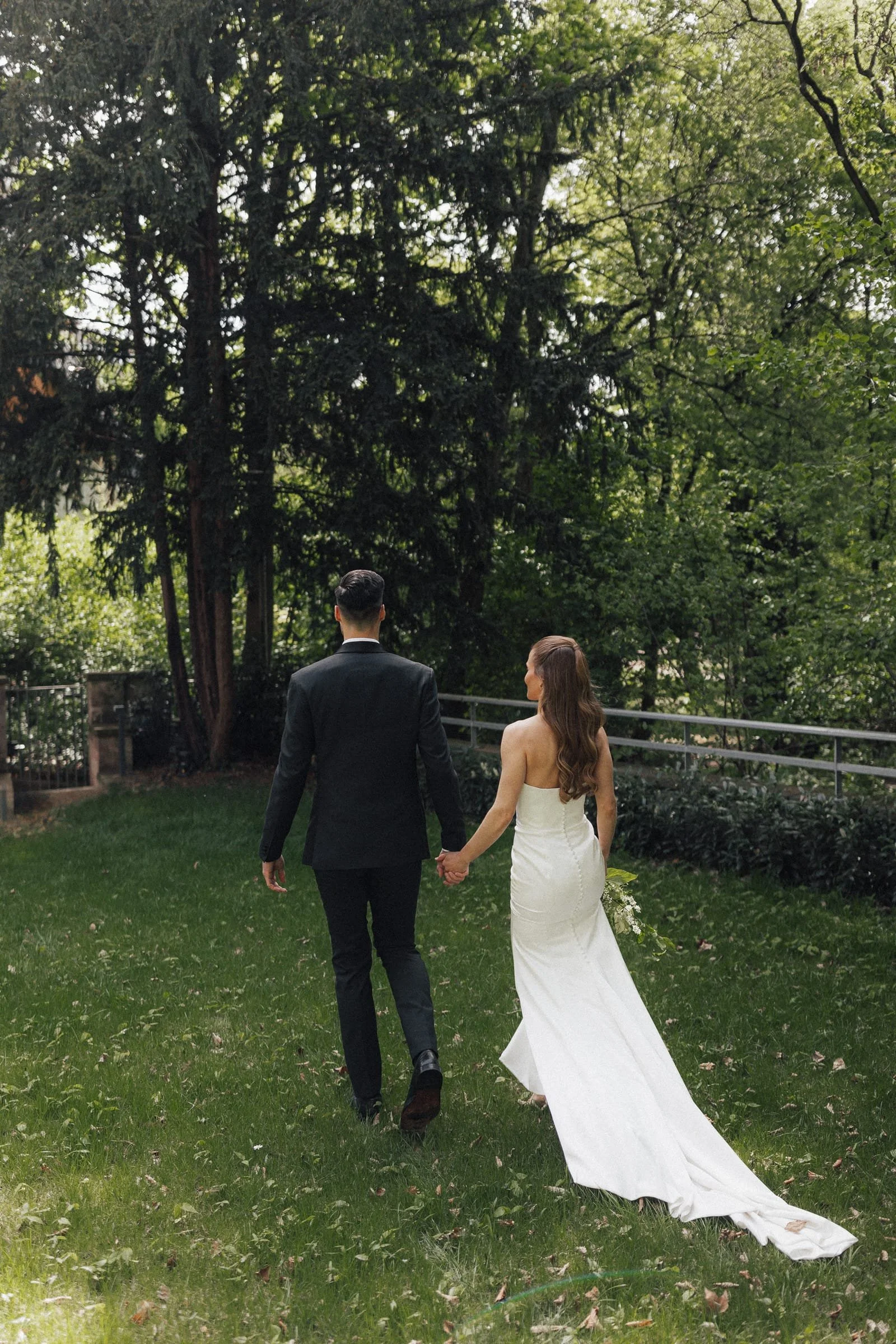 Braut und Bräutigam spazieren Hand in Hand durch einen grünen Garten bei ihrer Hochzeit.