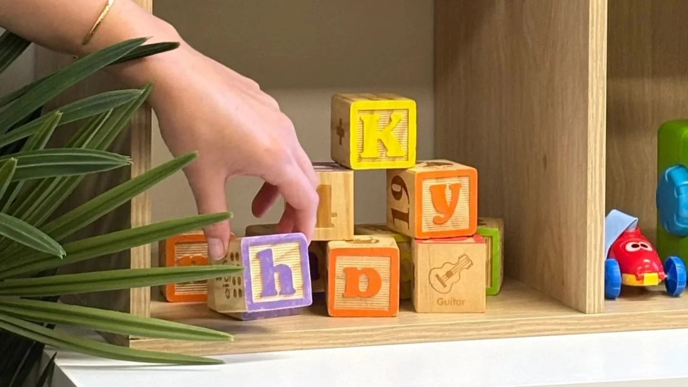 A hand reaching for wooden letter blocks on a shelf of toys at Therapy for Kids Perth.