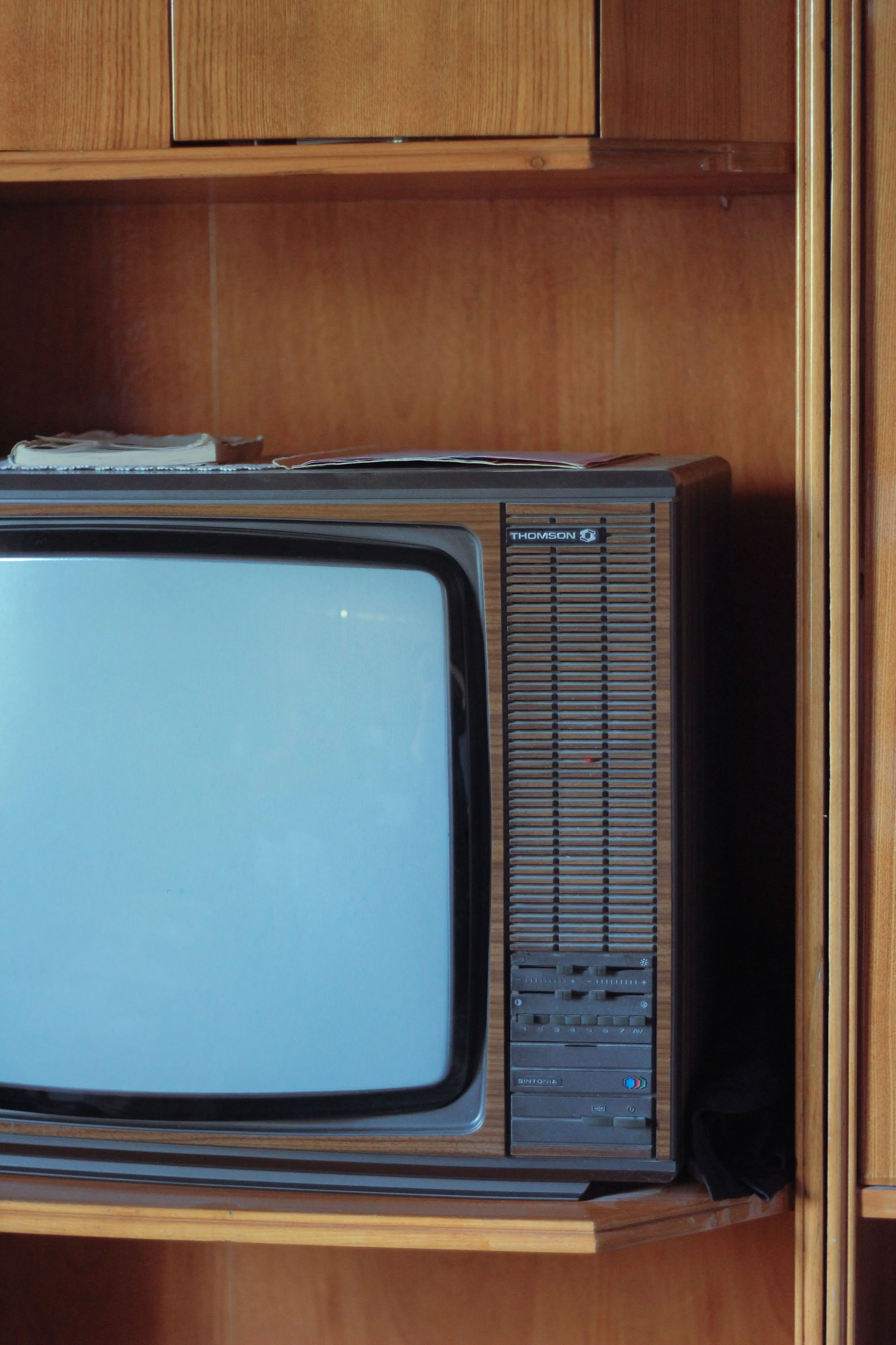 Close up photo of a corner of a vintage television with a walnut style casing and wooden wall behinf