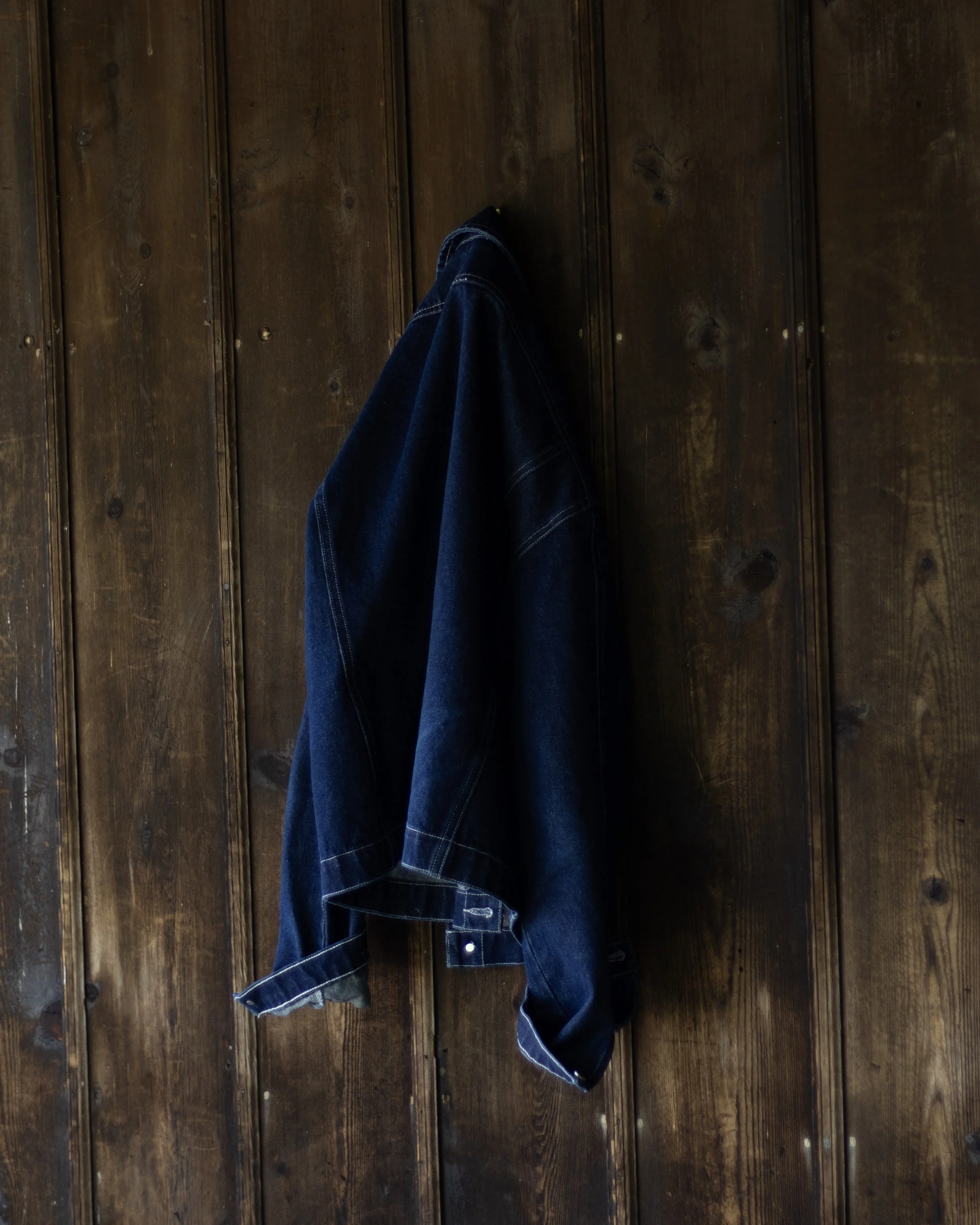 A person wearing dark blue jeans with rolled-up cuffs, standing on a wooden floor with visible wood grain and knots.