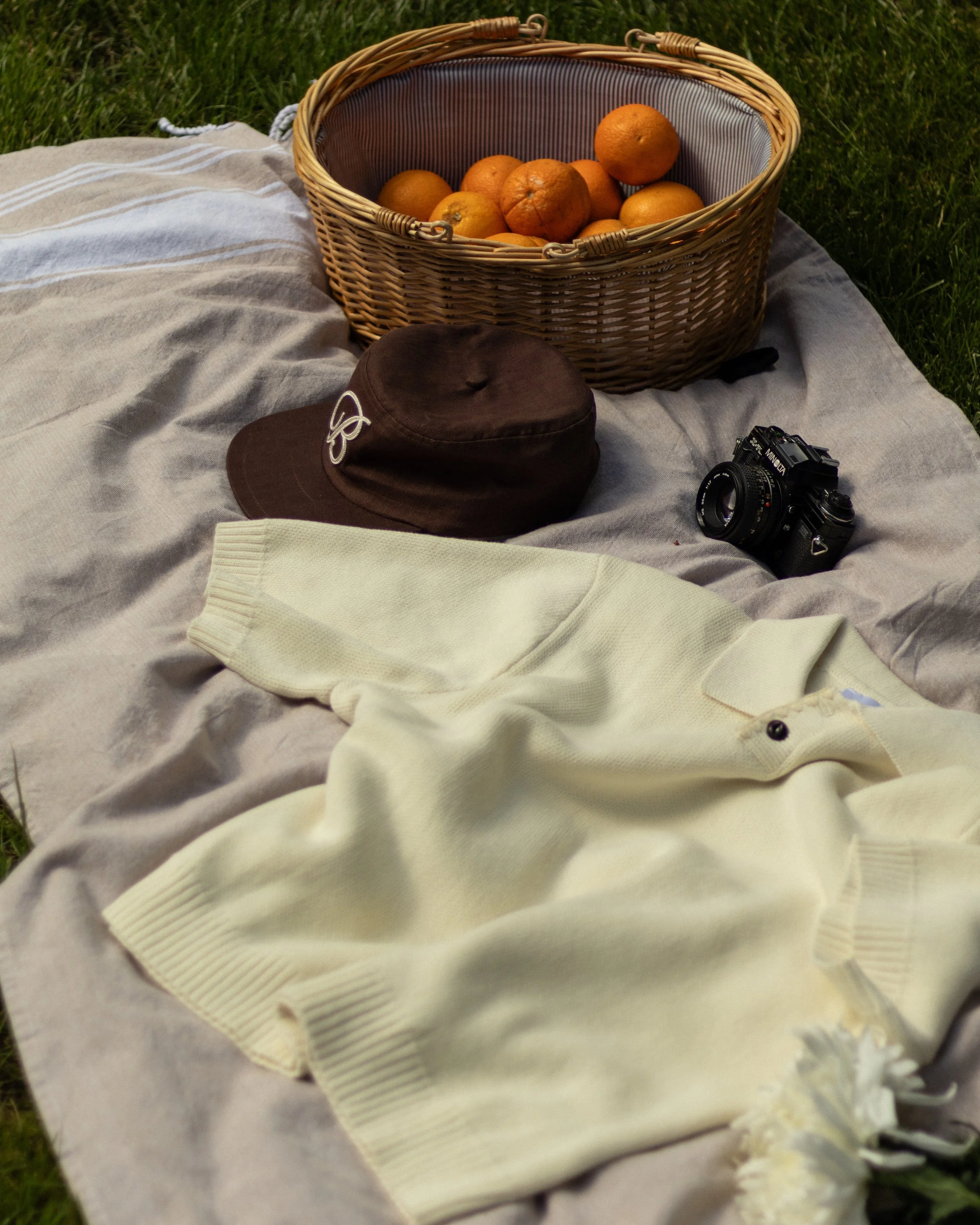 A wicker basket filled with oranges on a picnic blanket outdoors.