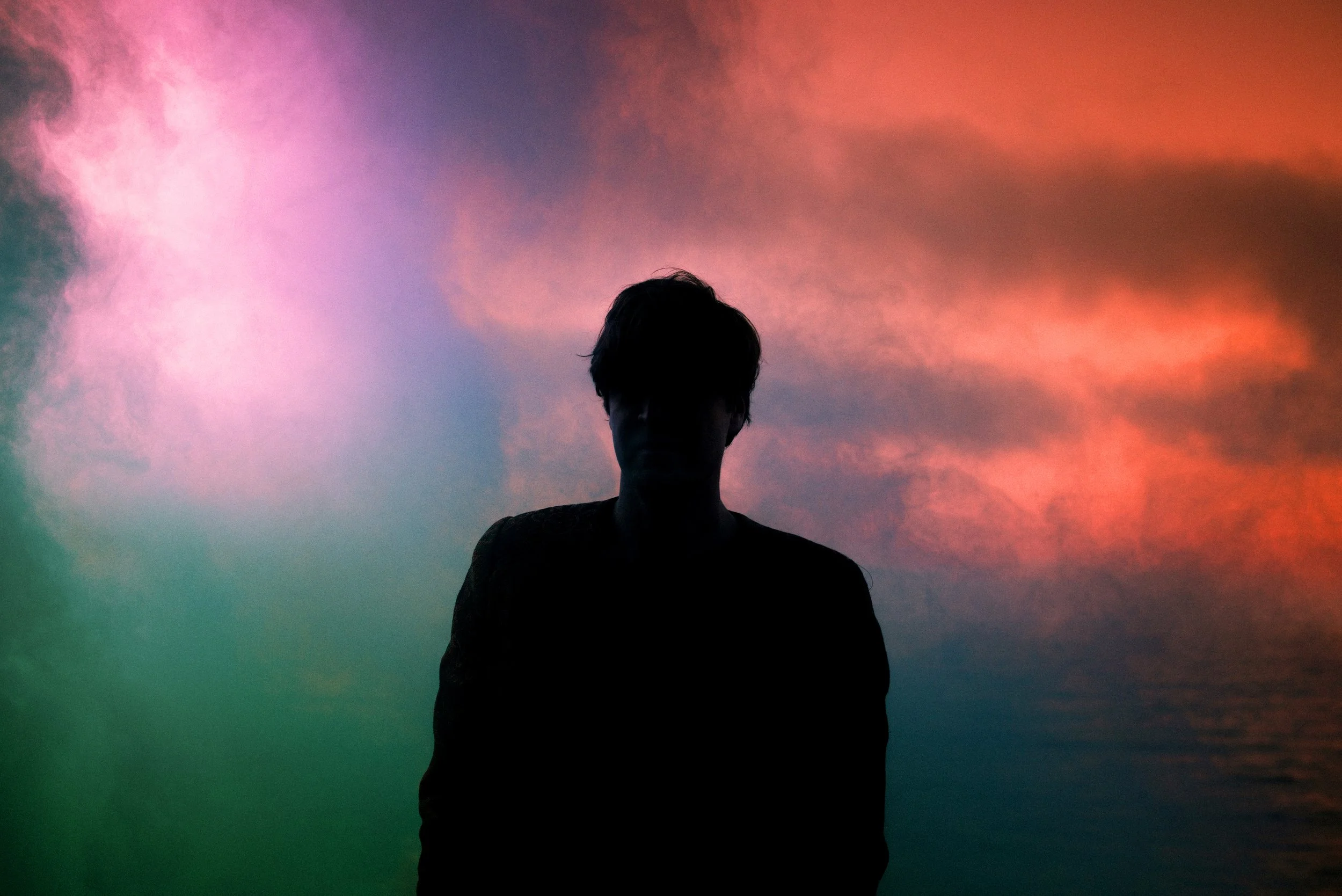 Schatten einer Person vor einem bunten, nebeligen Himmel bei Sonnenuntergang.