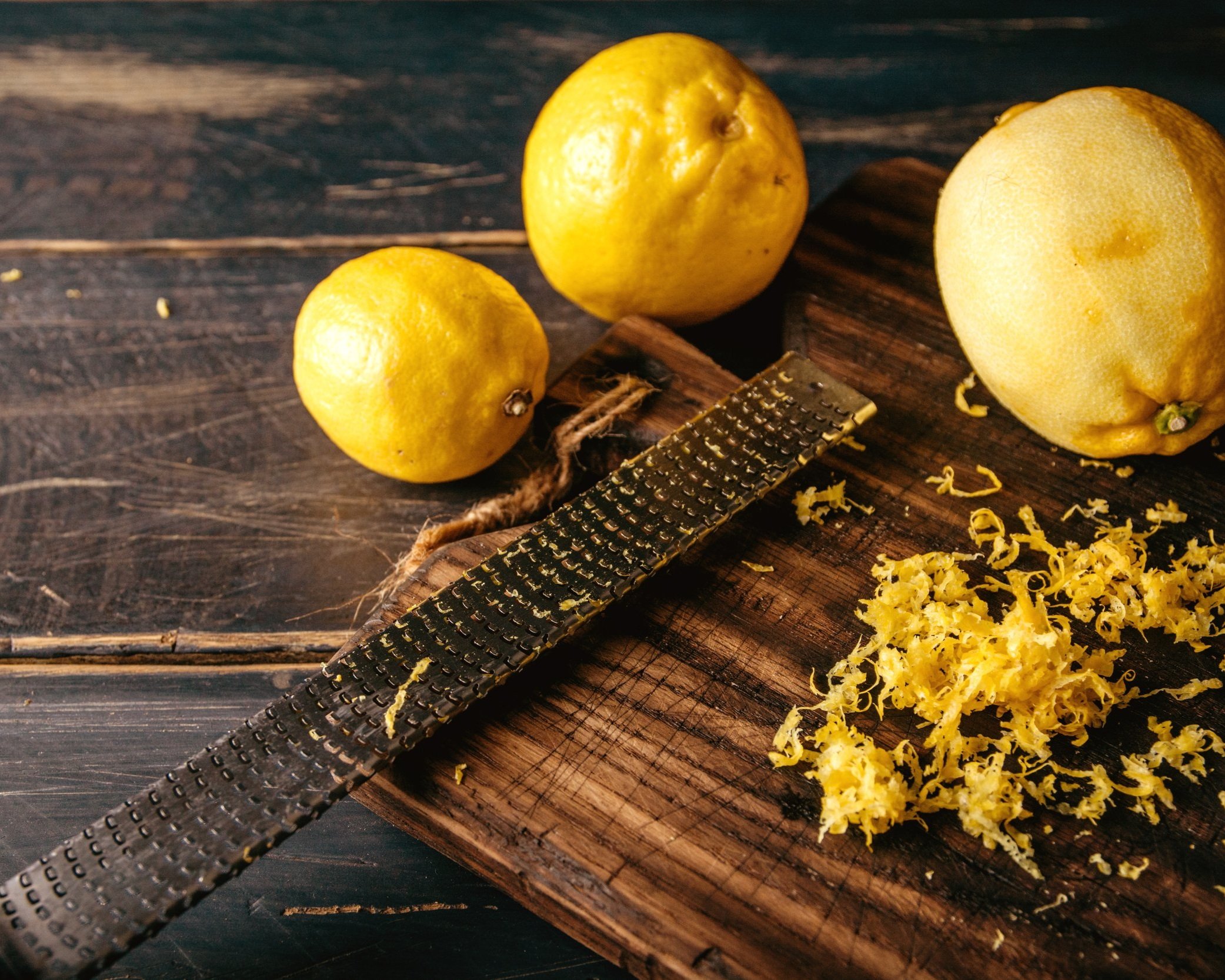 Limoni gialli su un tagliere di legno con una grattugia e scorze di limone grattugiate.