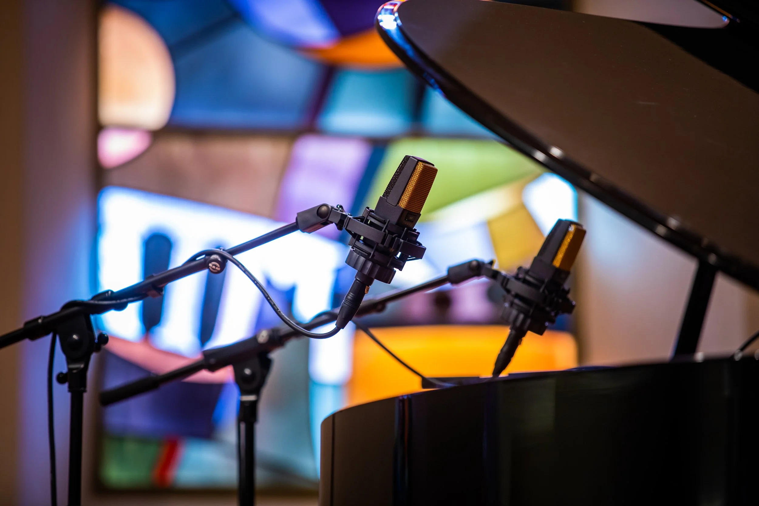 Paire de microphones à condensateur devant un piano à queue et un vitrail