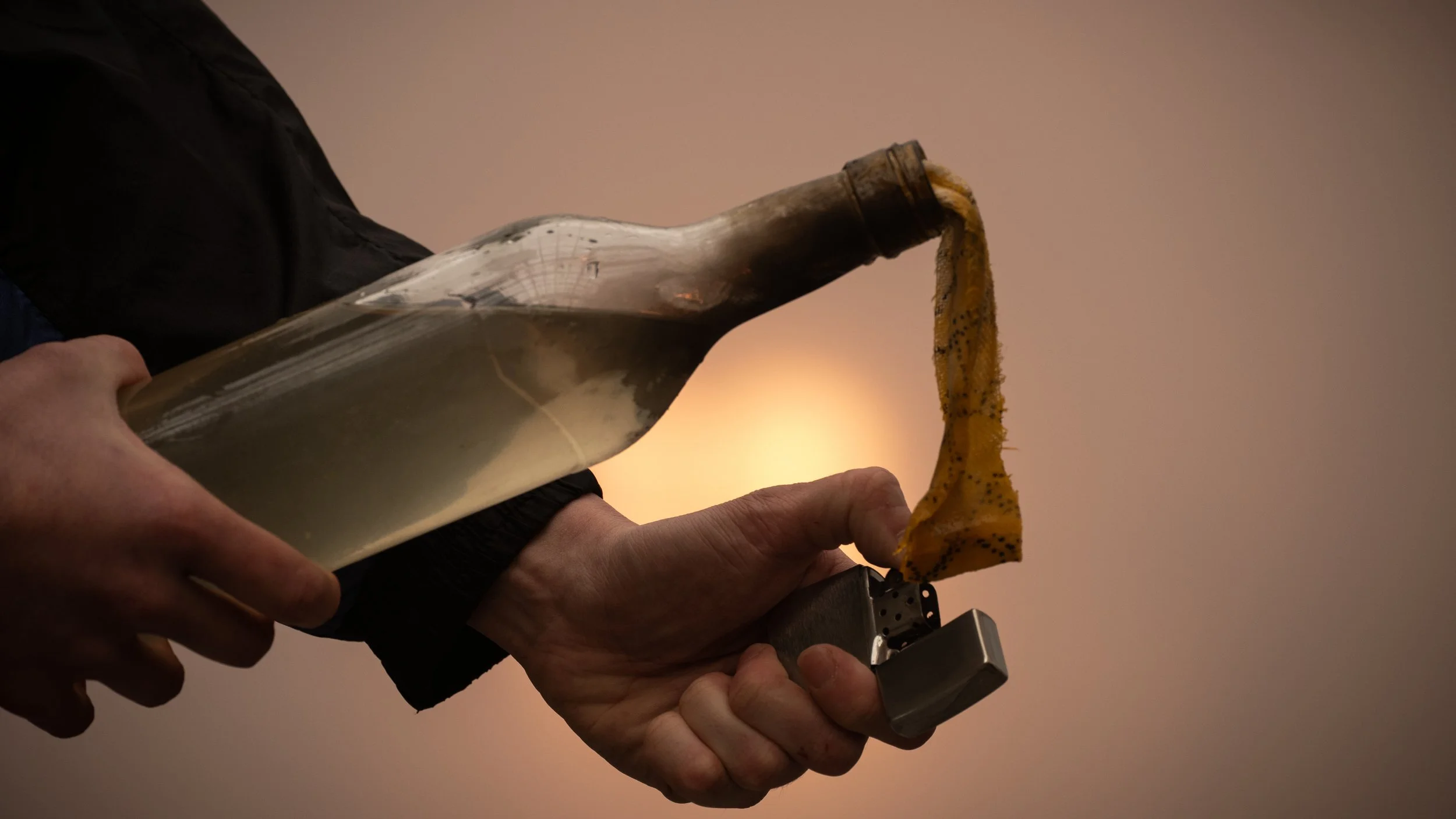 Une personne tient une bouteille en verre à moitié remplie, versant de la gelée ou un liquide jaune avec des graines noires sur un briquet