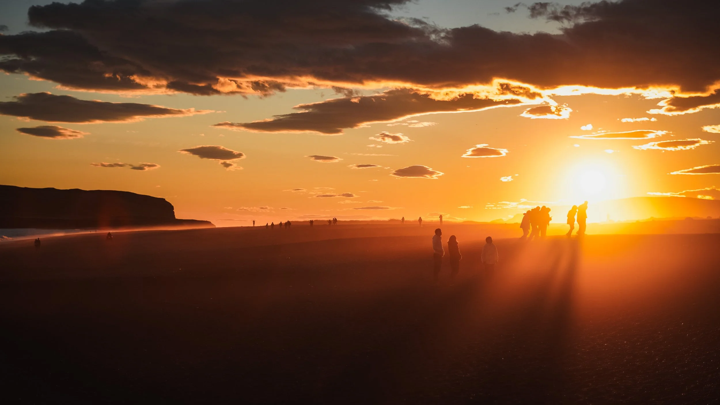 Coucher de soleil sur une plage avec des silhouettes de personnes et des formations rocheuses au fond