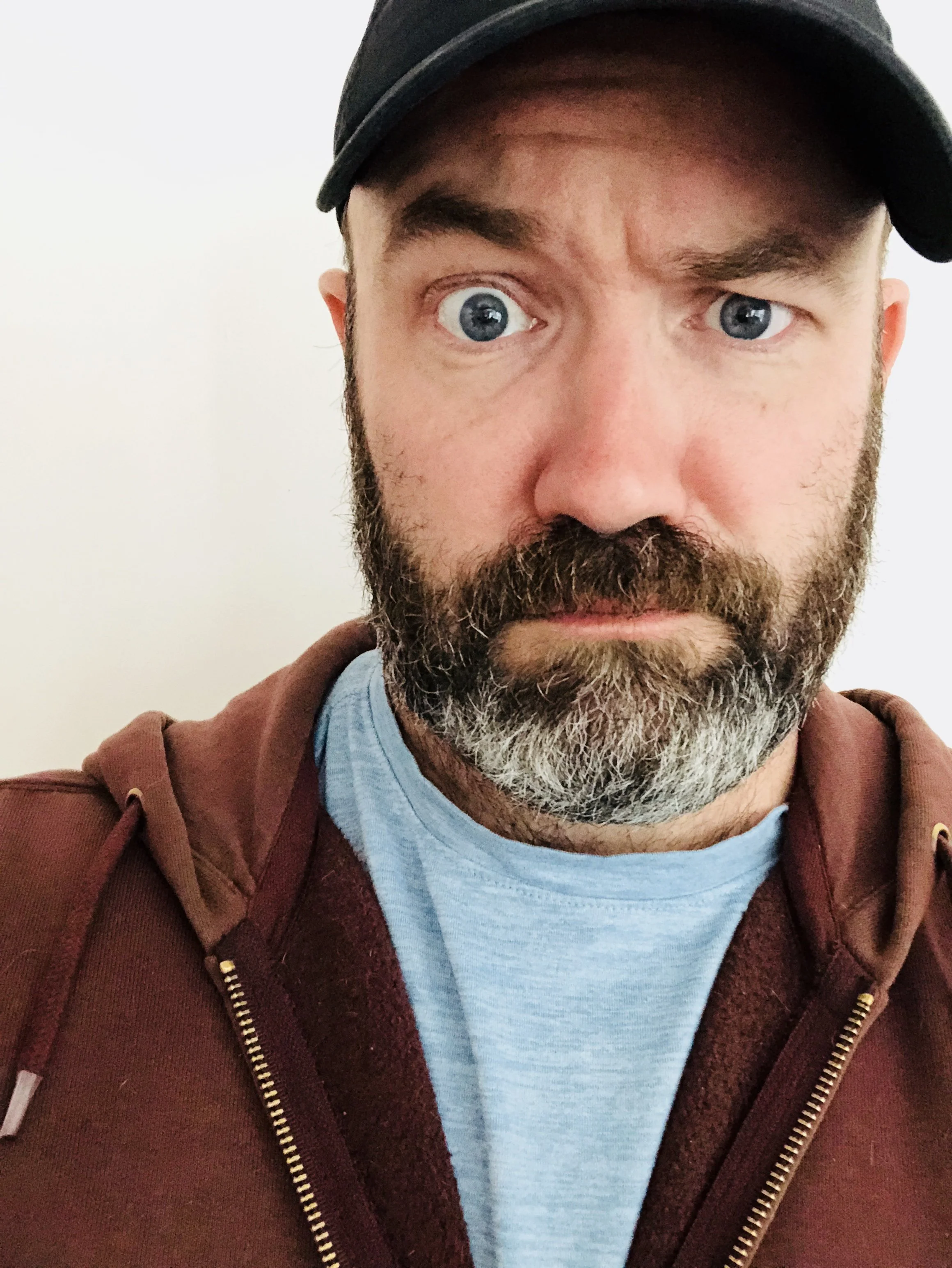 confused looking man in a maroon sweatshirt and light blue tee, with a salt-and-pepper beard