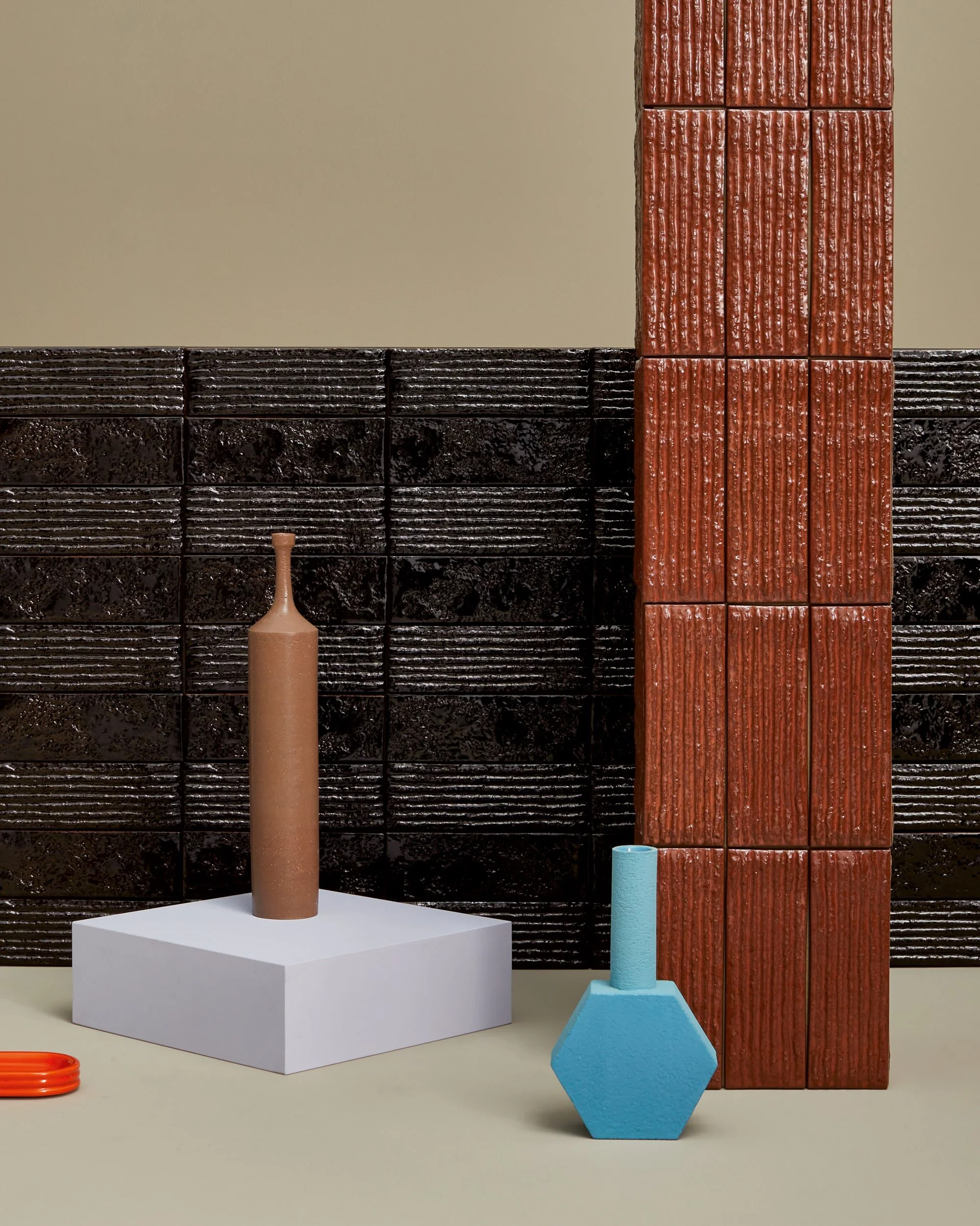 Skulpturale Keramikvase und geometrische Skulpturen auf einer weißen und beige Oberfläche vor dekorativen Fliesenwänden in Schwarz und Rot.