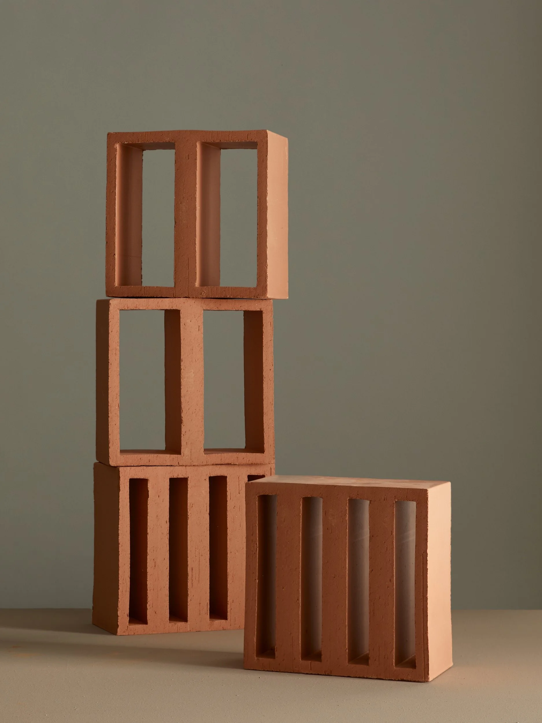 Drei ziegelartige Steine, zwei auf dem Boden und einer darauf, gegen eine graue Wand.