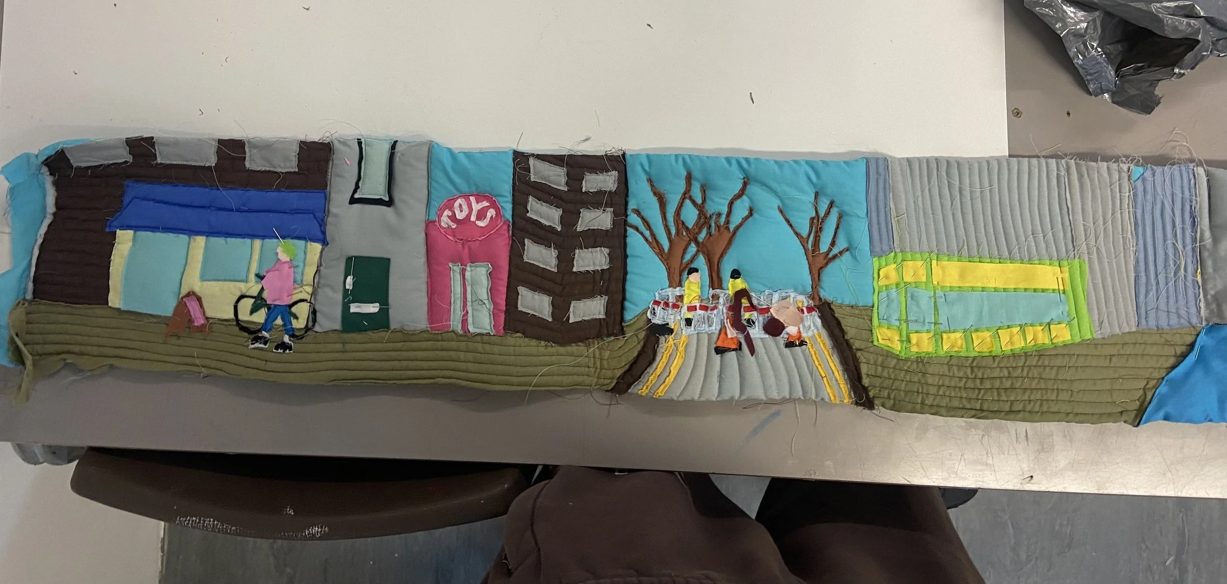 Sewn art showing a street with shops and people