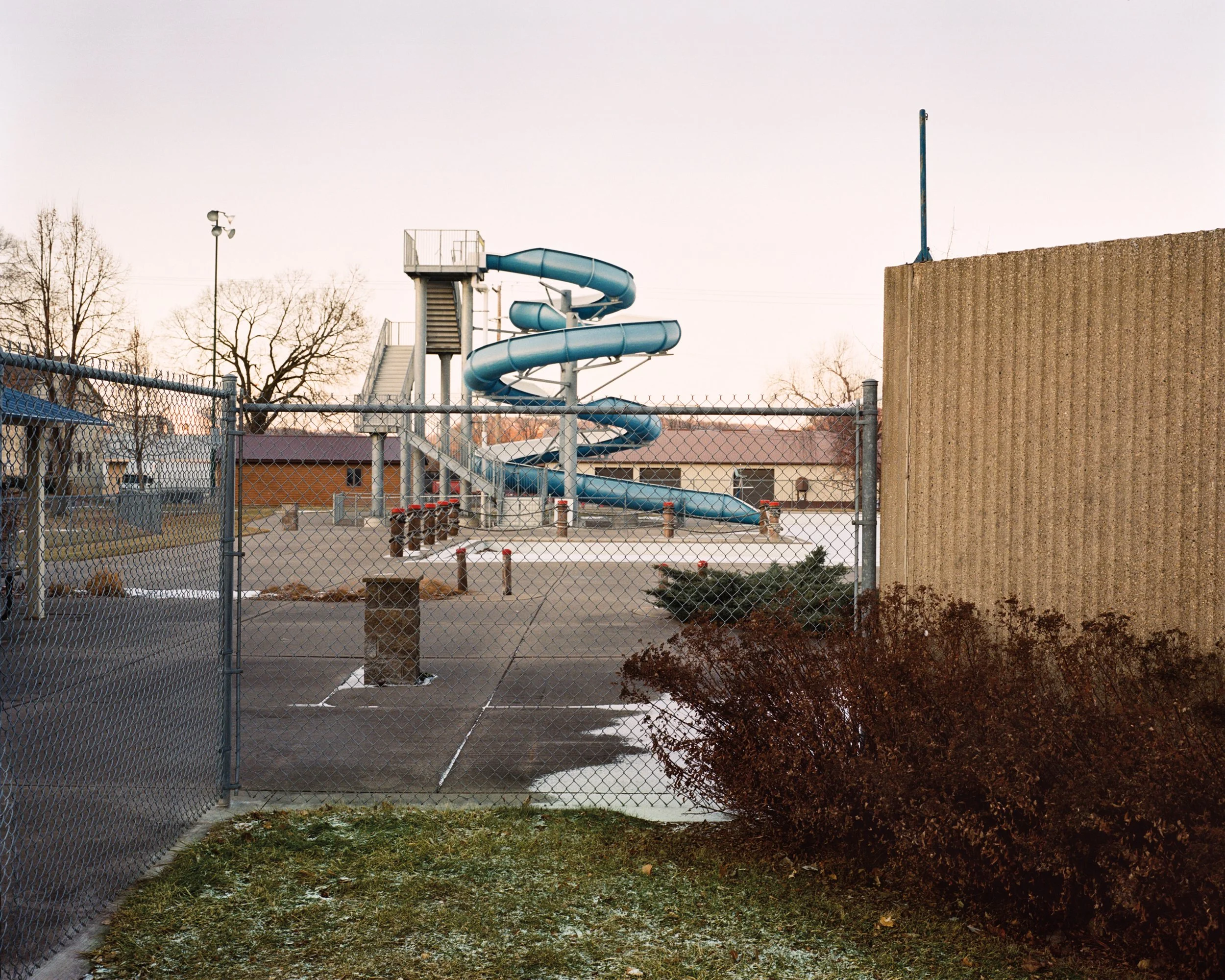Tobogán en espiral de color azul detrás de una verja de eslabones en un parque vacío