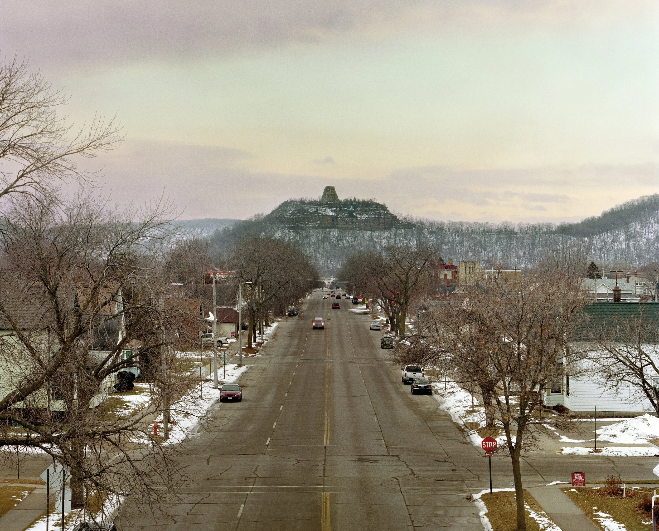 Autos en una calle arbolada que se dirigen hacia un gran peñasco en el fondo