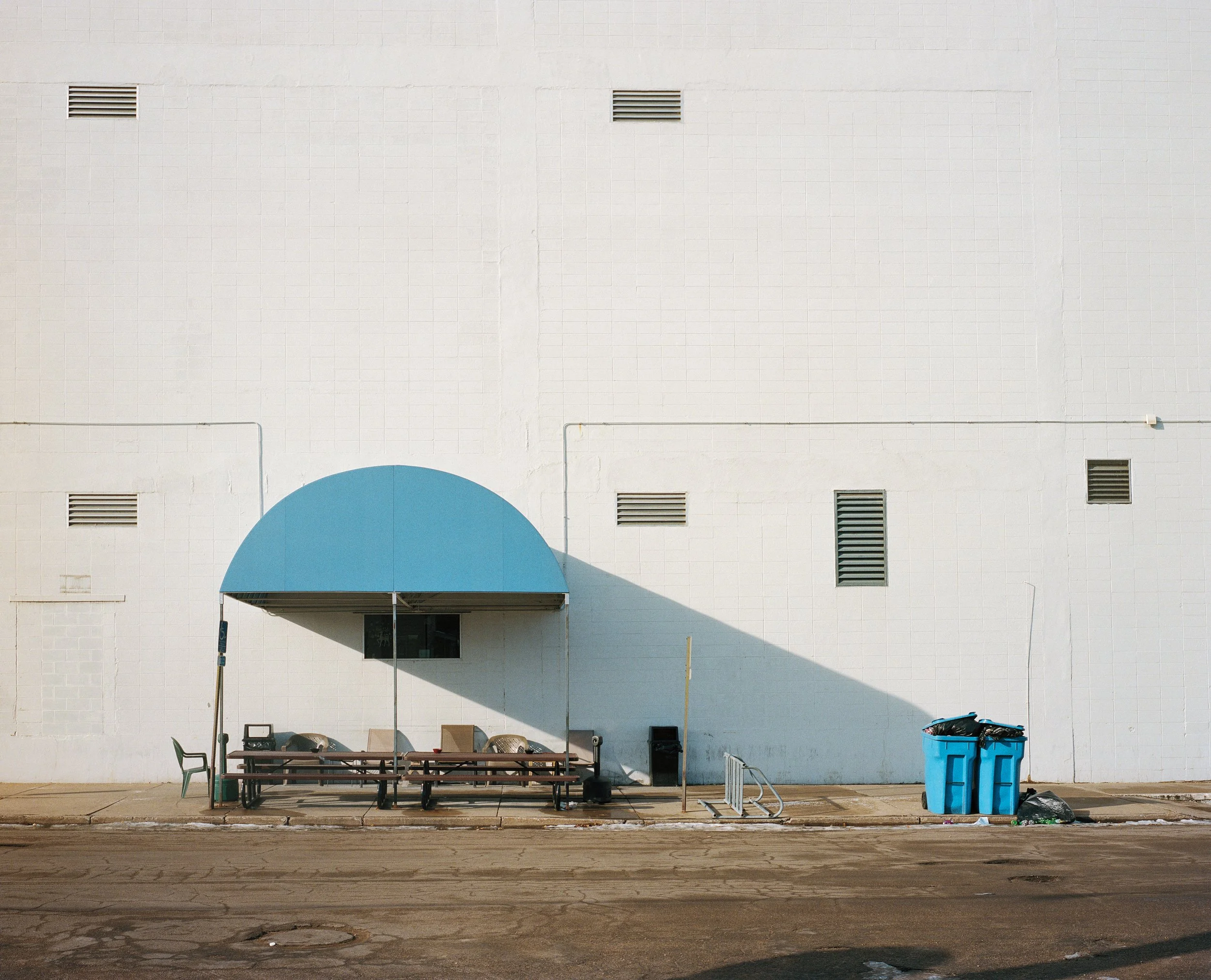 Sillas y mesa bajo un toldo azul cerca de cubos de basura de color azul