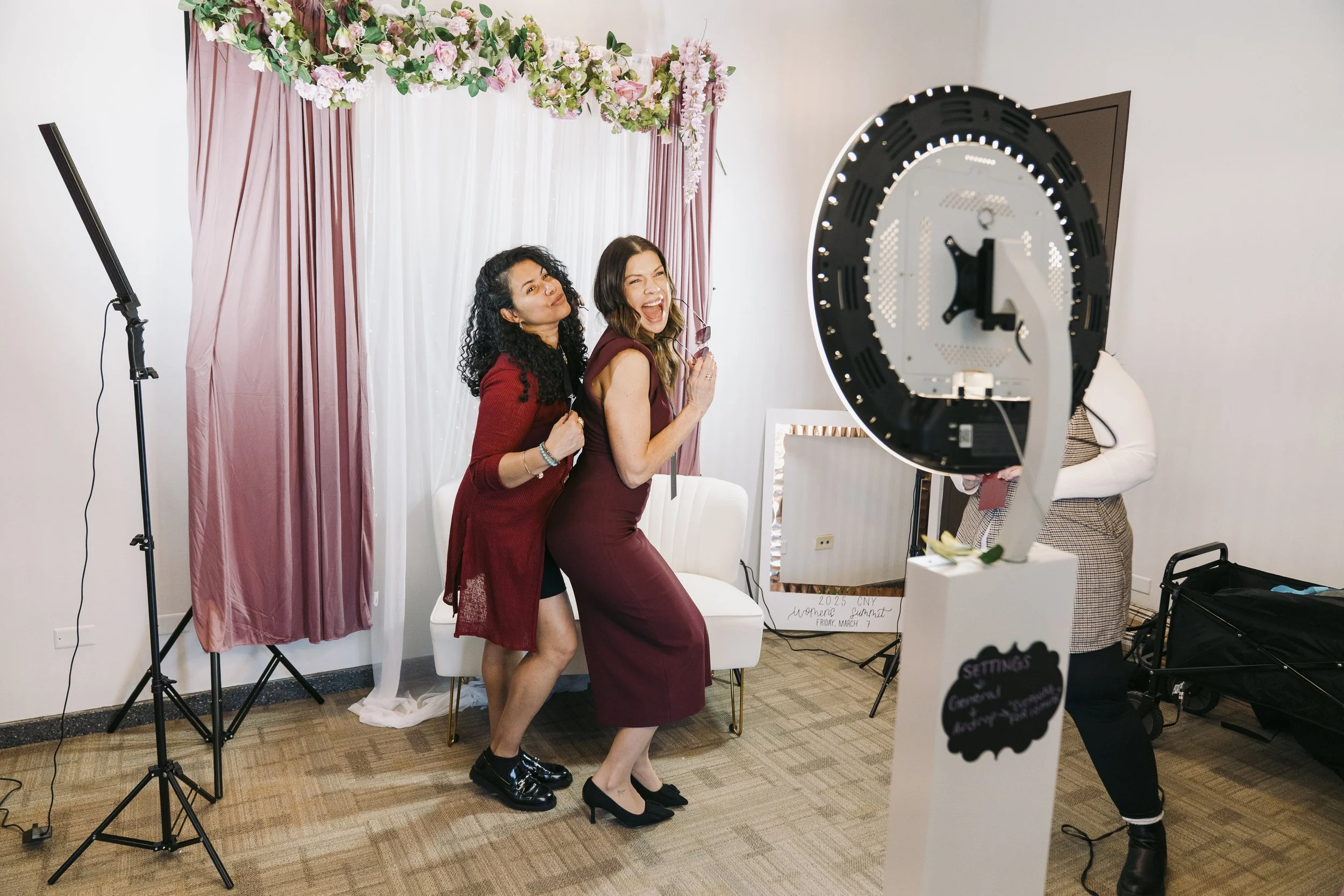 two women pose at a photo booth at the CNY Womens Summit