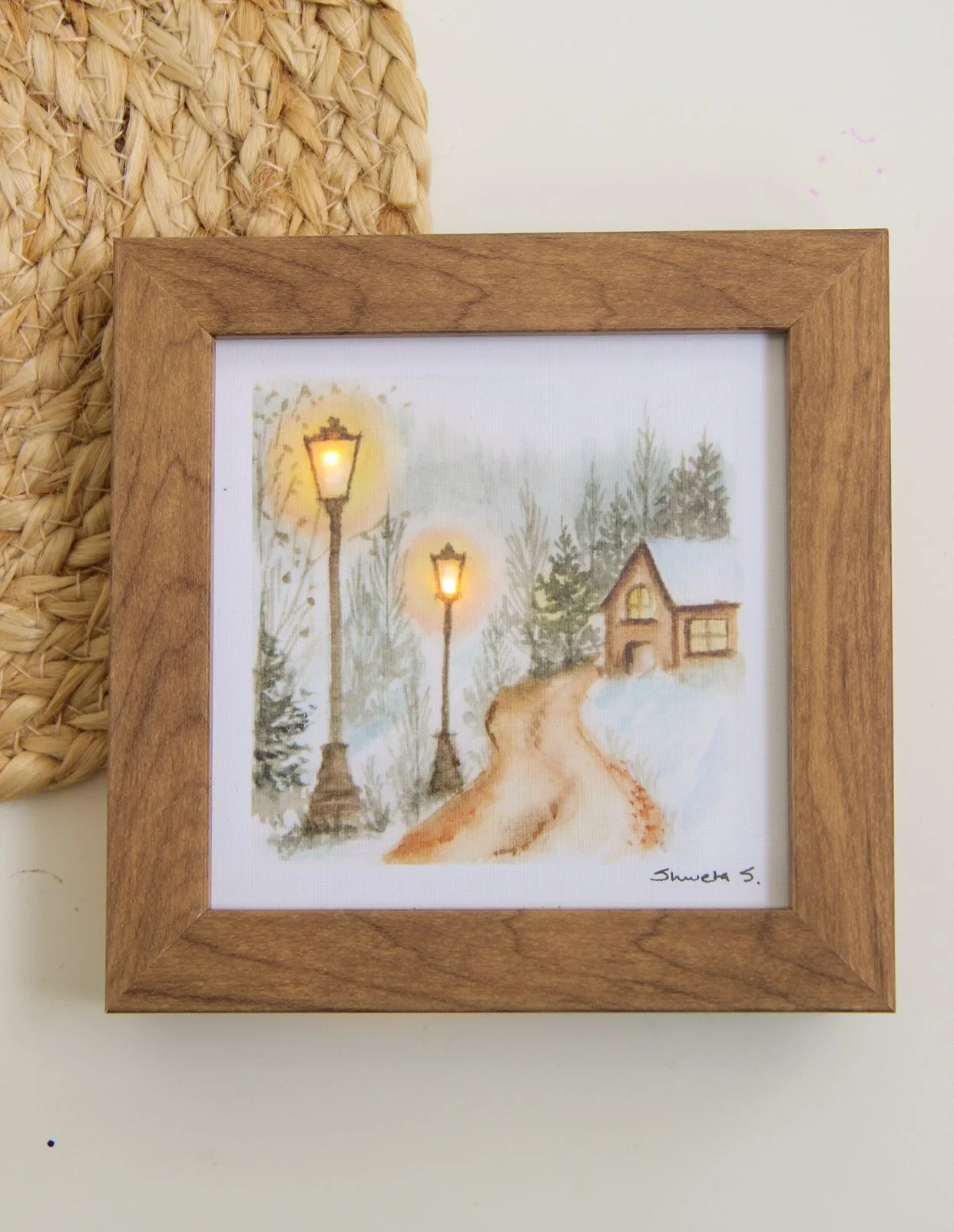 Light-up winter art print showing a snow-covered cottage under a glowing street lamp.