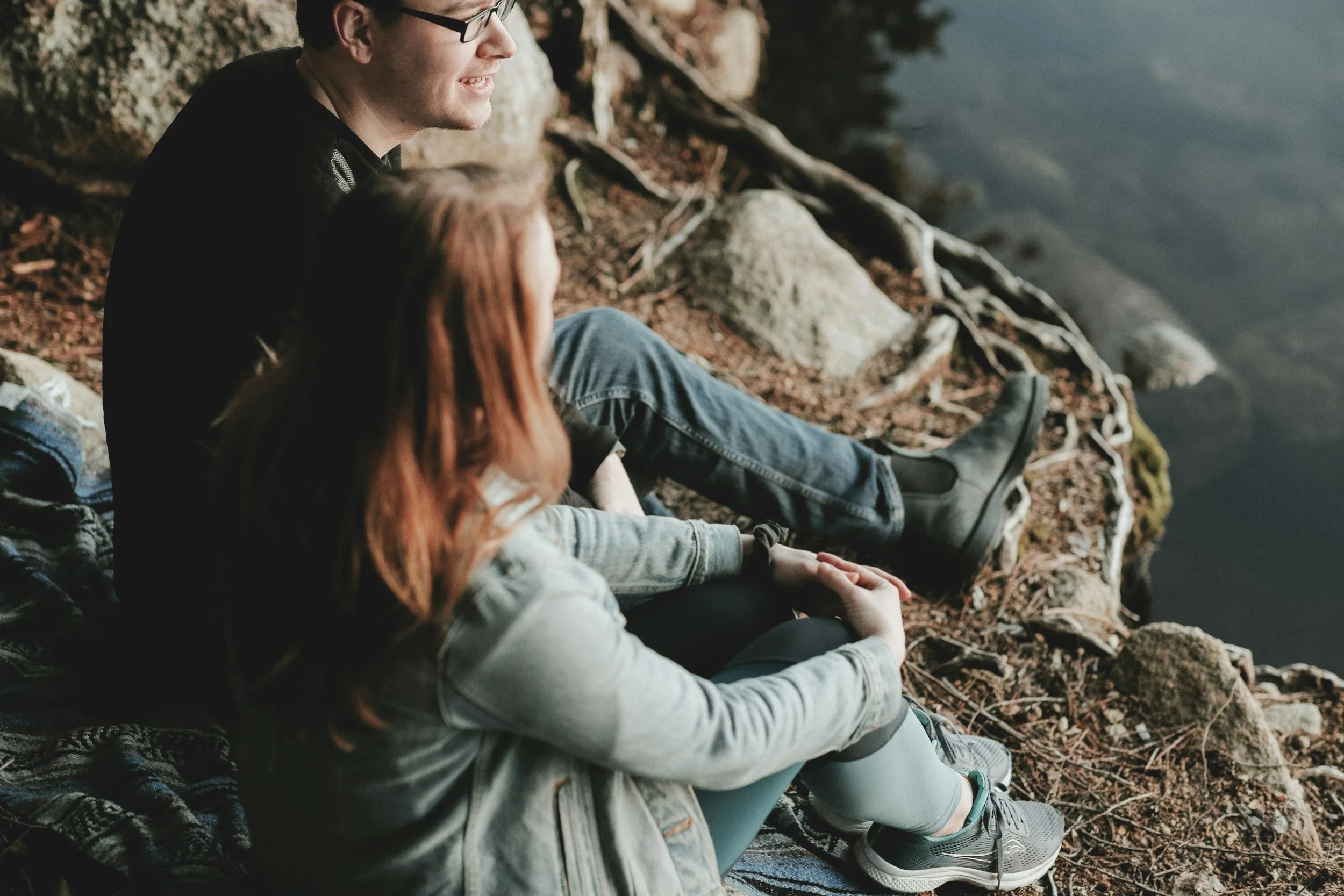 Three people sitting by a lake on a rocky and wooded shoreline, enjoying nature.