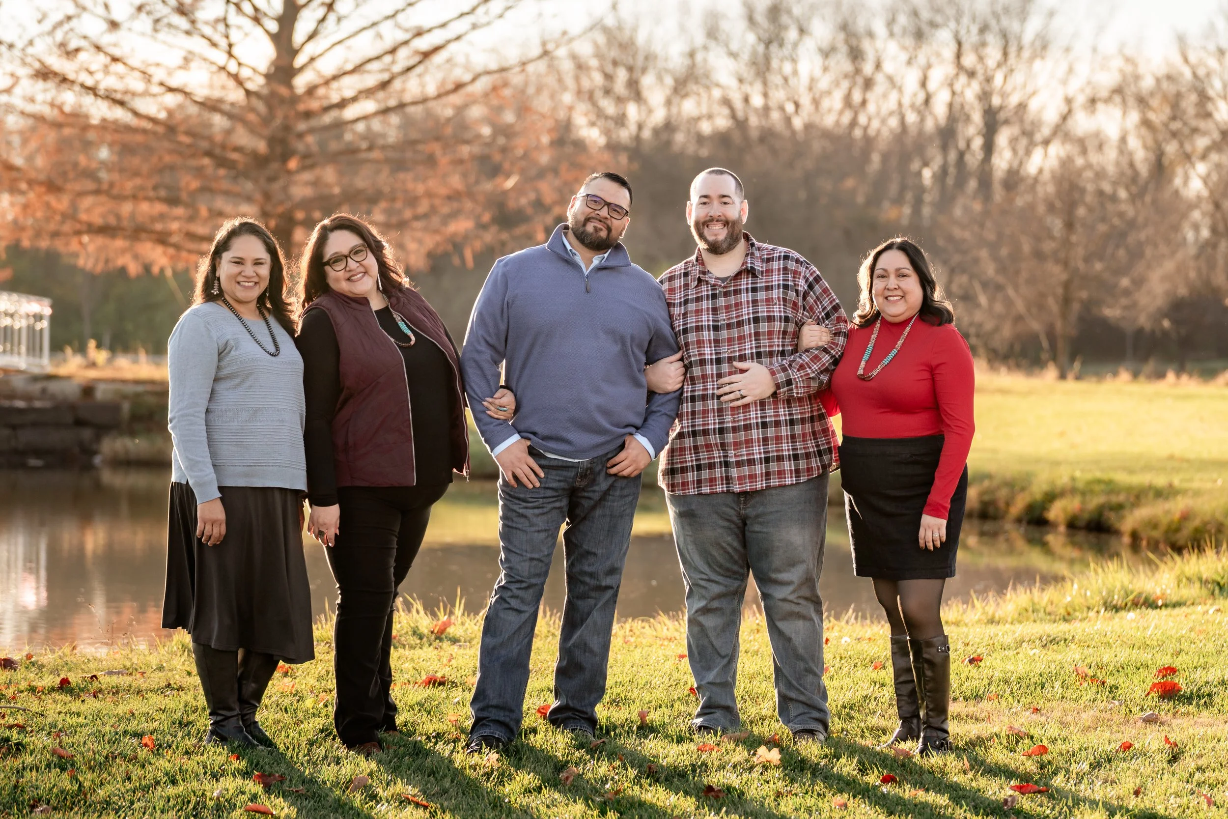A family of four posing outdoors in a field of tall grass during autumn, smiling at the camera.