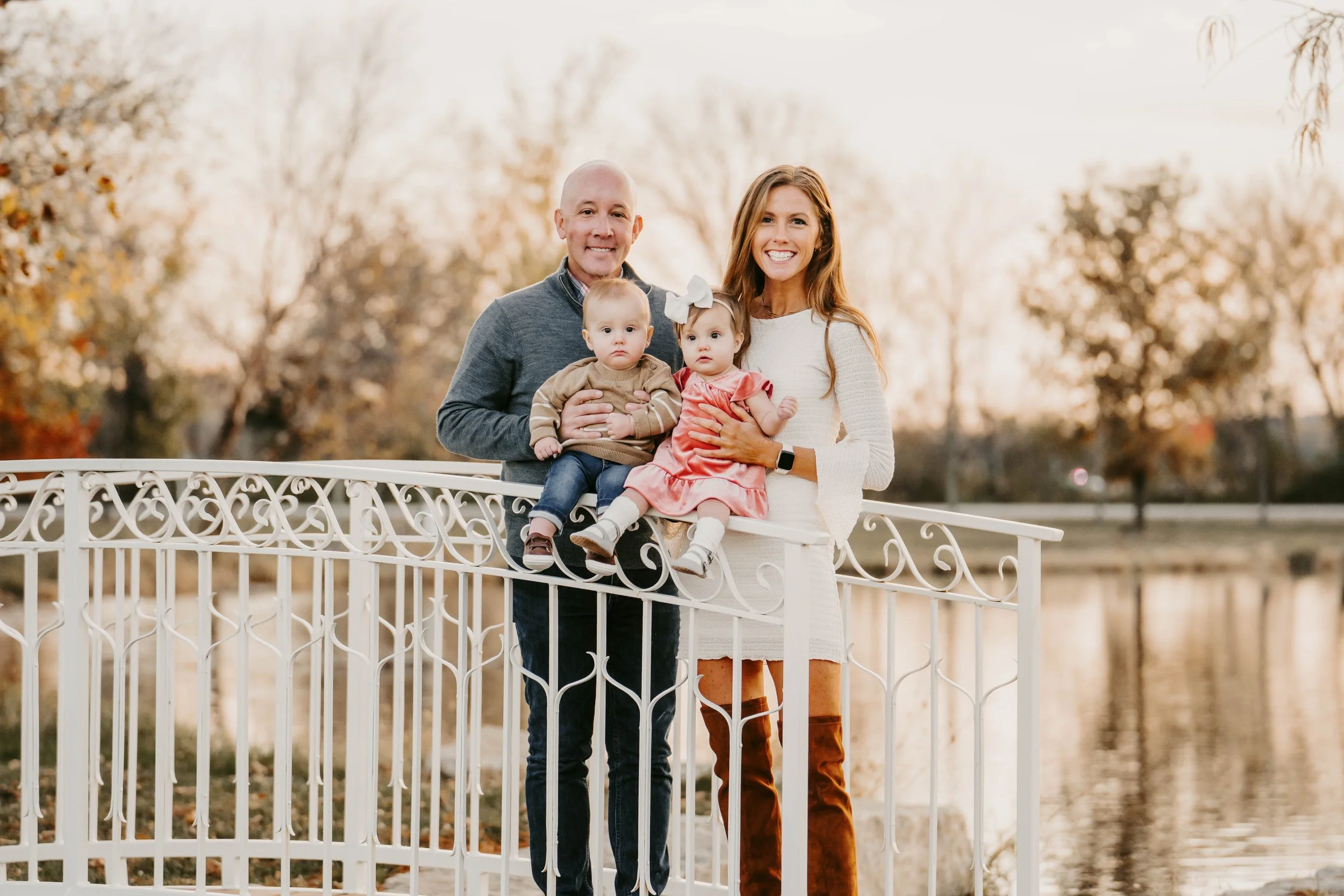 Family of four smiling on a railing near water during fall