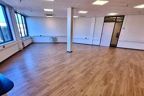 Lege kantoorruimte met grote ramen en gereinigde vloer na renovatie.