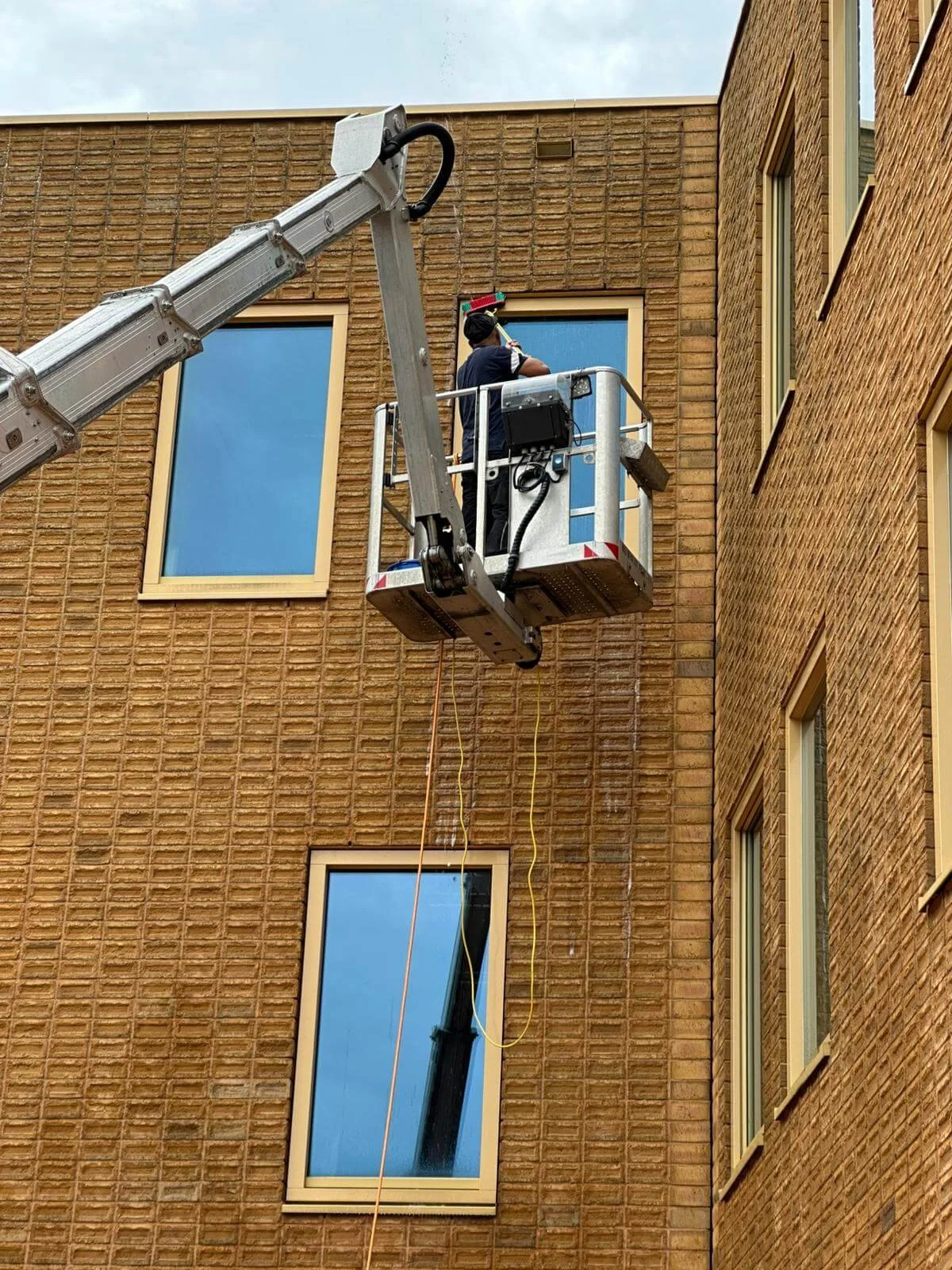 Glazenwasser werkt vanuit een hoogwerker aan ramen van een appartementencomplex.