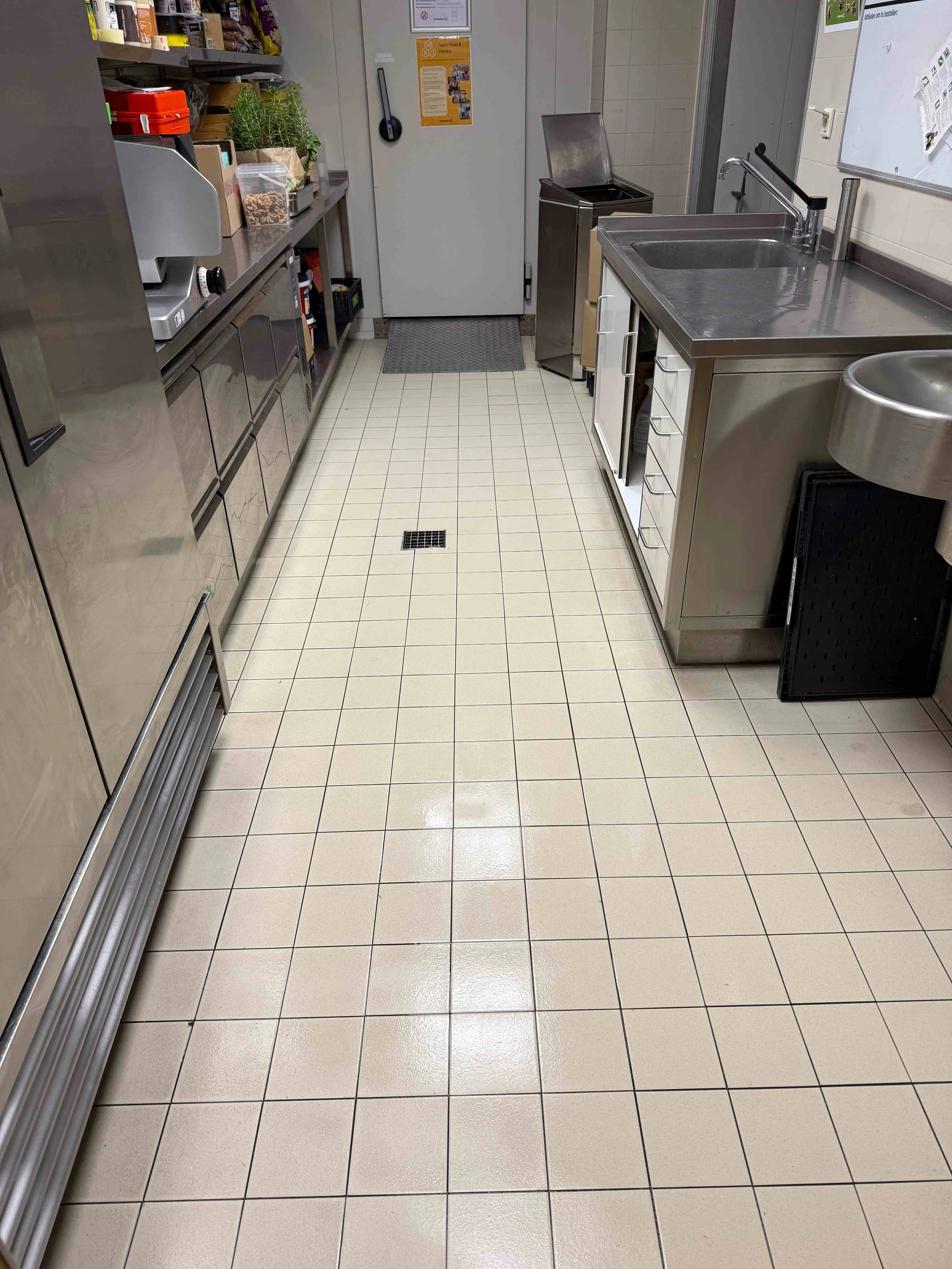 Professionele keuken met roestvrijstalen werkbladen, spoelbakken en tegelvloer.