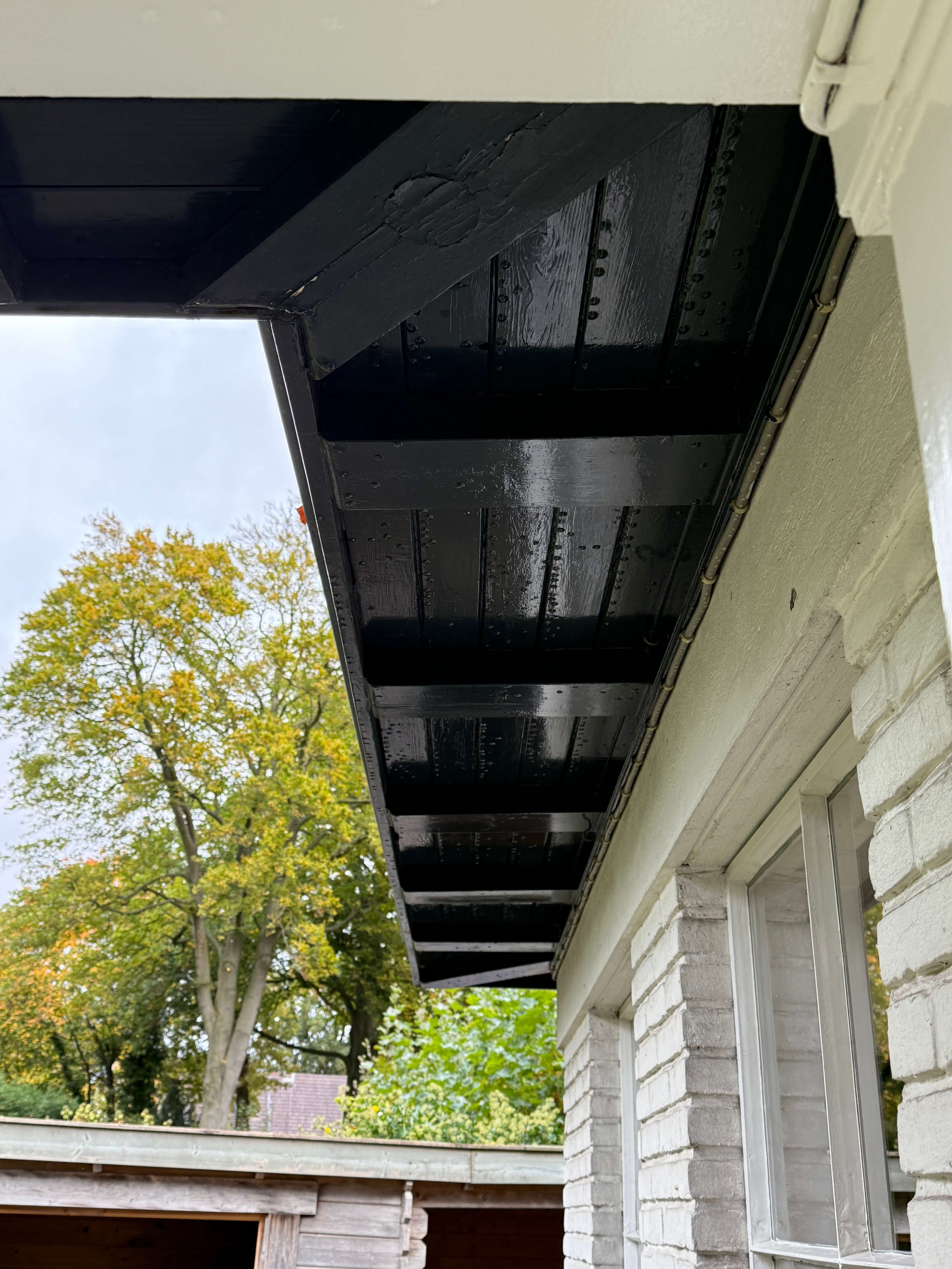 Donker geschilderd houten dakoverstek met zichtbare planken en draagbalken.