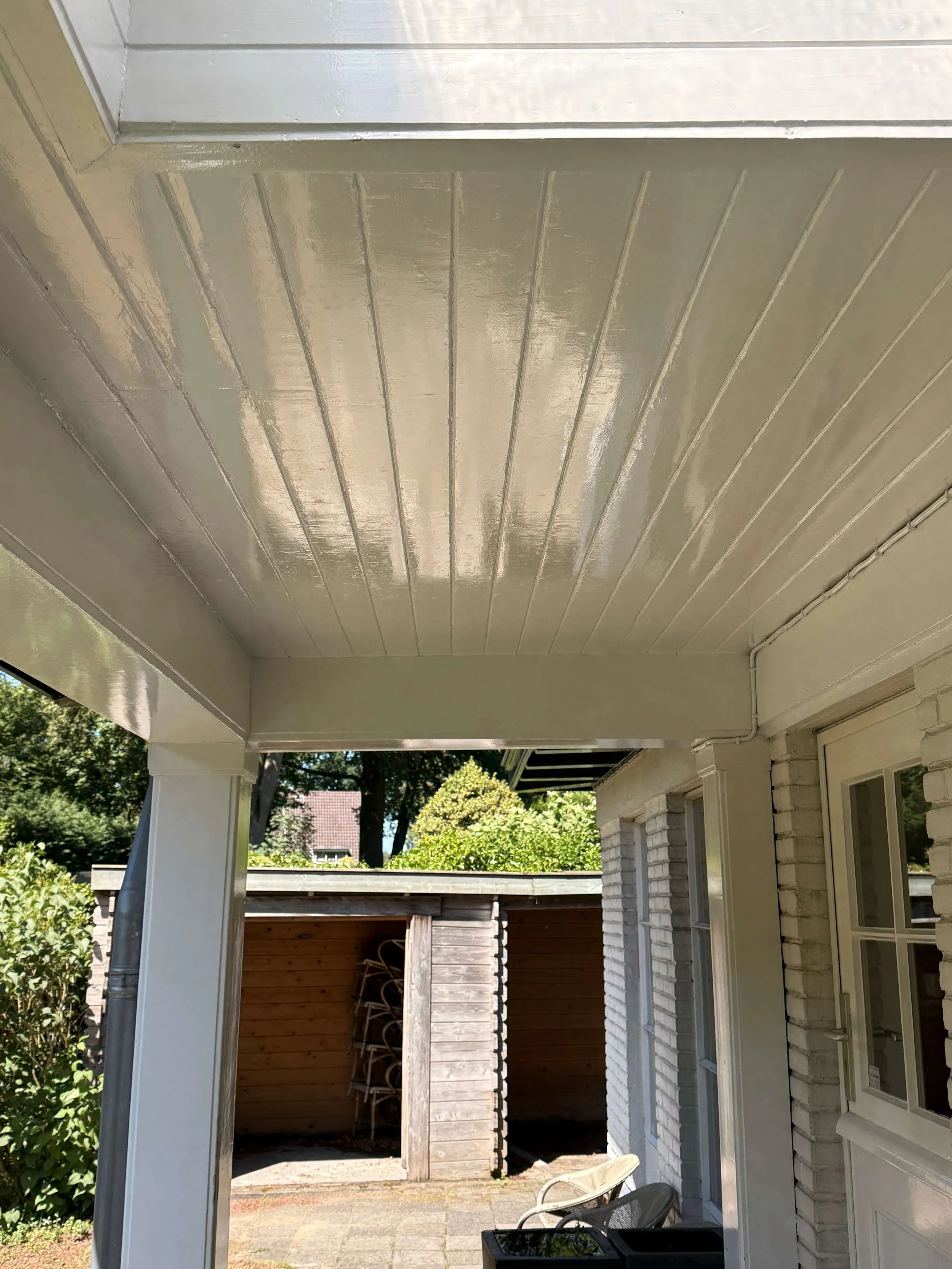 Wit plafond en dakoverstek van een overdekte buitenruimte met zichtbare houten panelen.