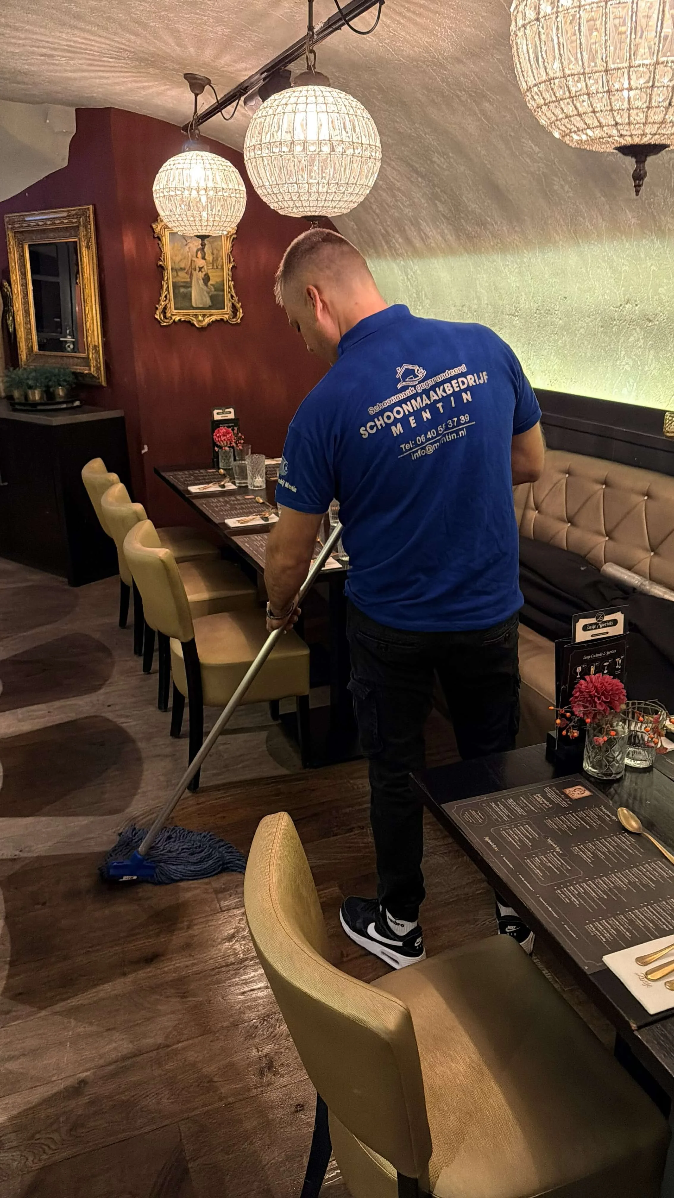 Schoonmaker van Mentin dweilt de vloer tussen de tafels in een restaurant.