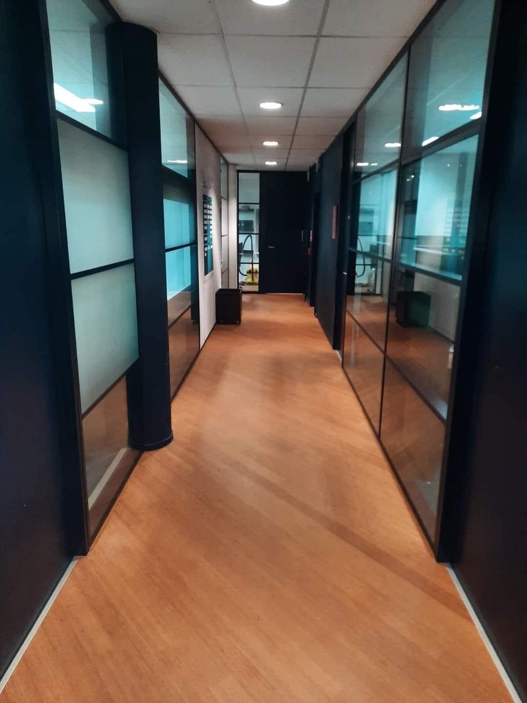 Kantoorgang met glazen scheidingswanden en een houten vloer.