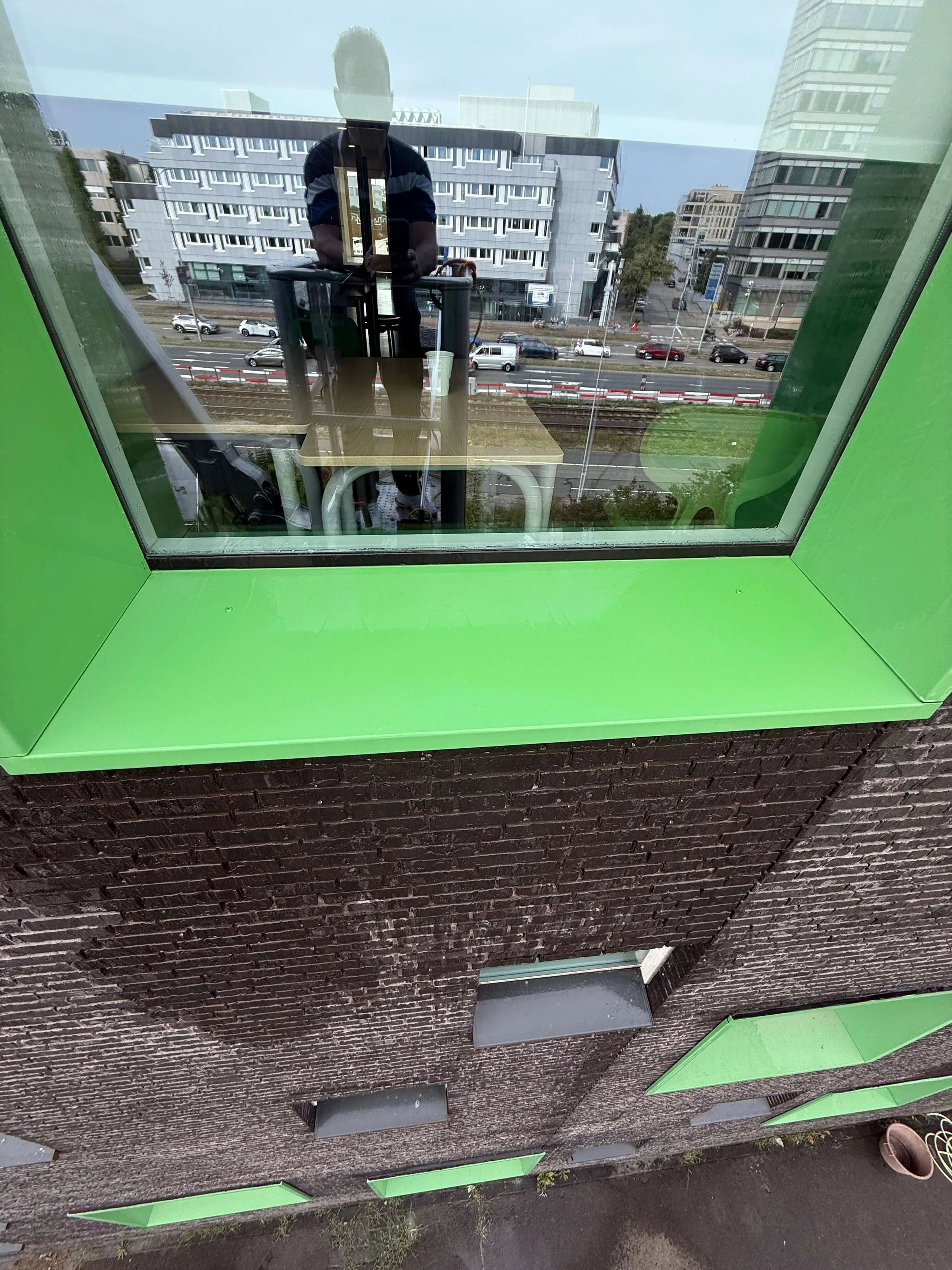 Schoon raam met groen kozijn en vensterbank aan een bakstenen gevel.