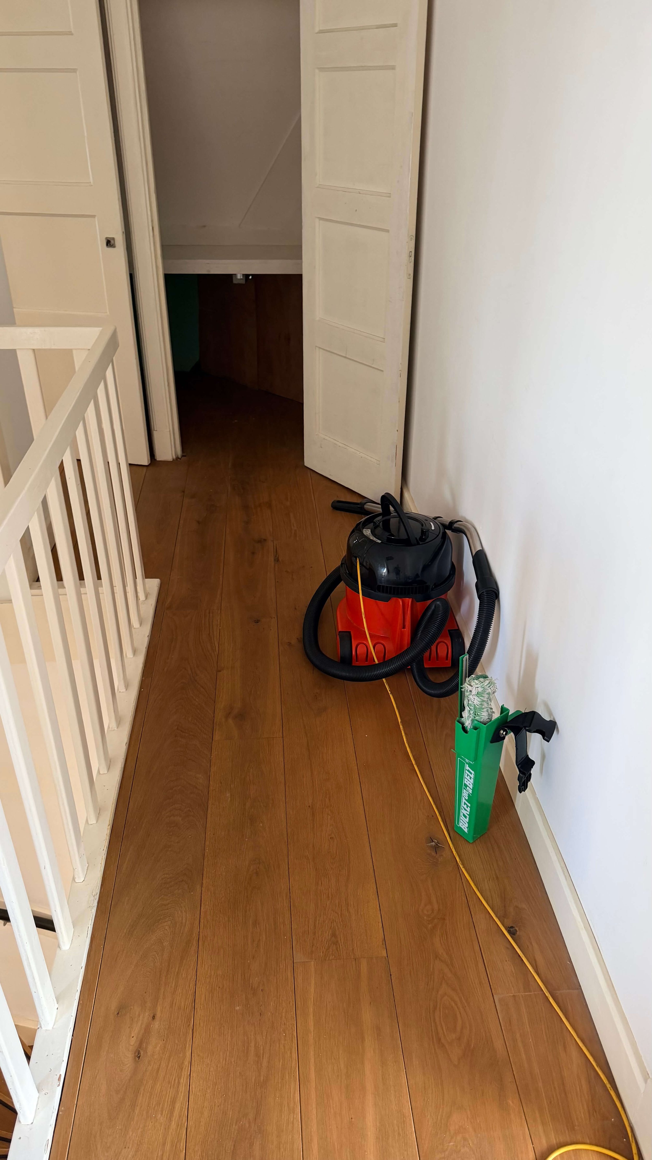 Professionele stofzuiger en schoonmaakmateriaal in een houten gang tijdens schoonmaakwerkzaamheden.