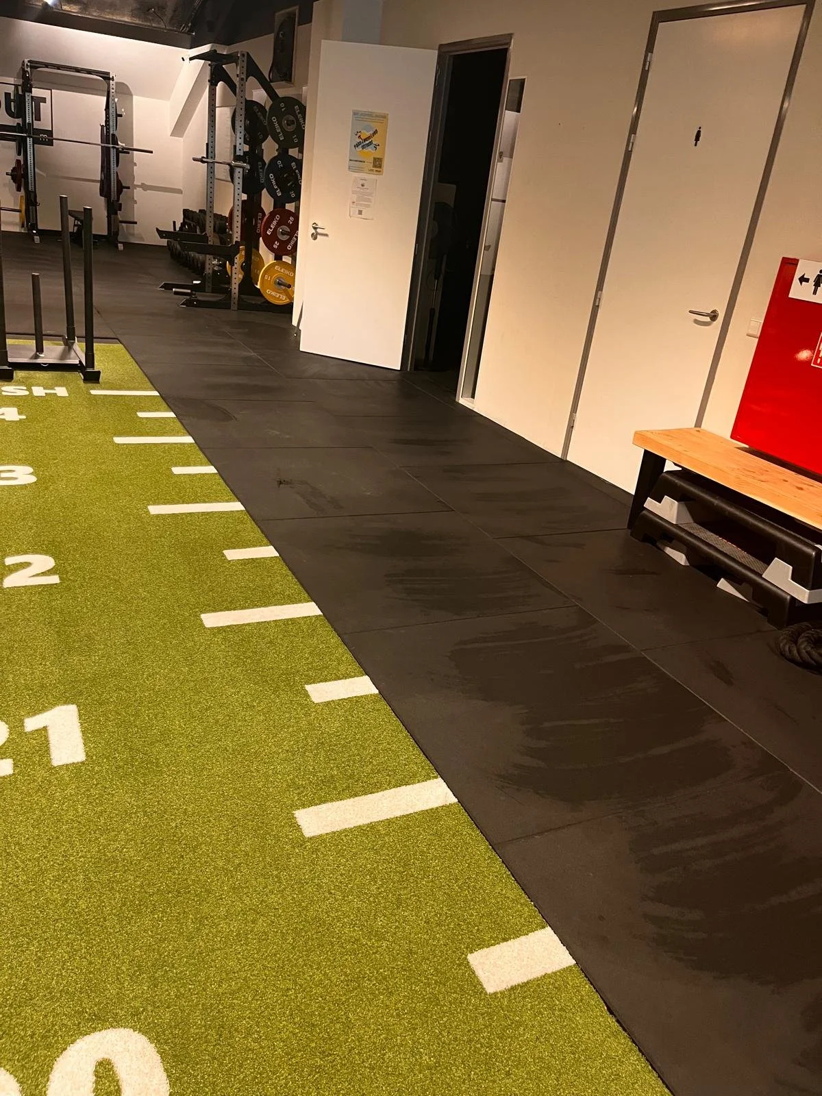 Rubberen sportvloer en groene trainingsmat in een fitnessruimte.