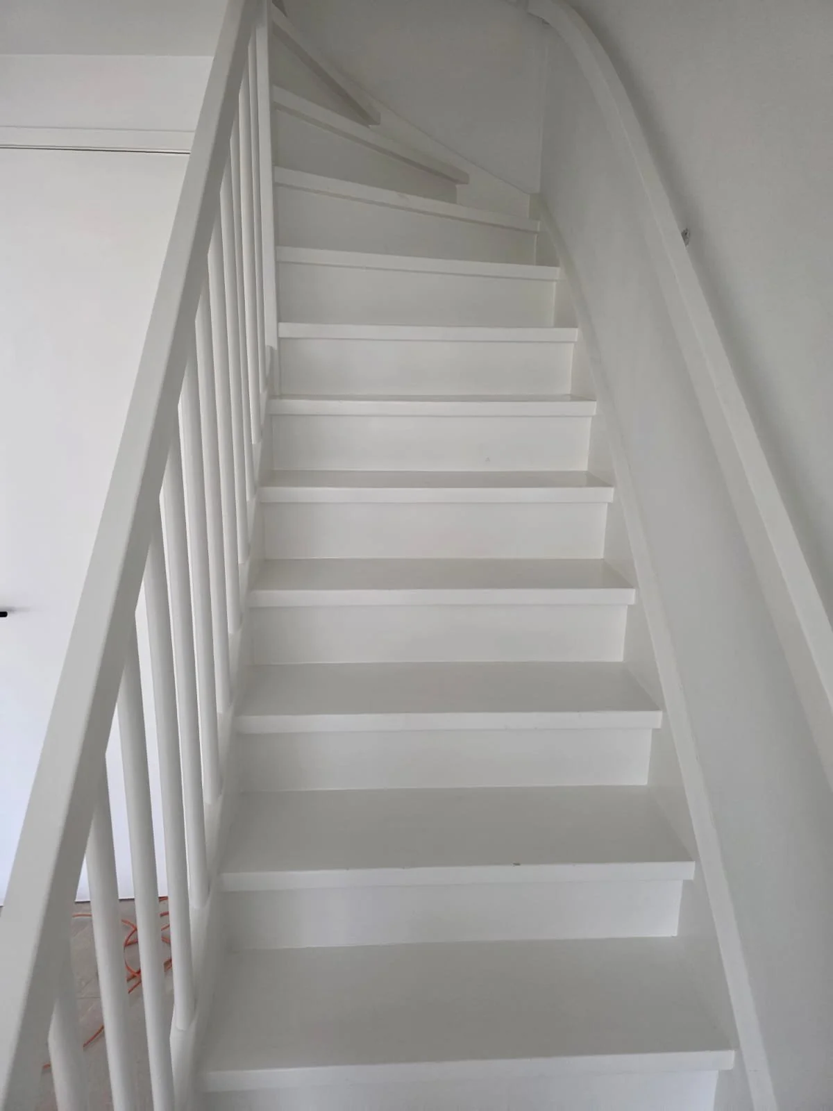 Witte binnentrap met witte leuningen en balustrade.