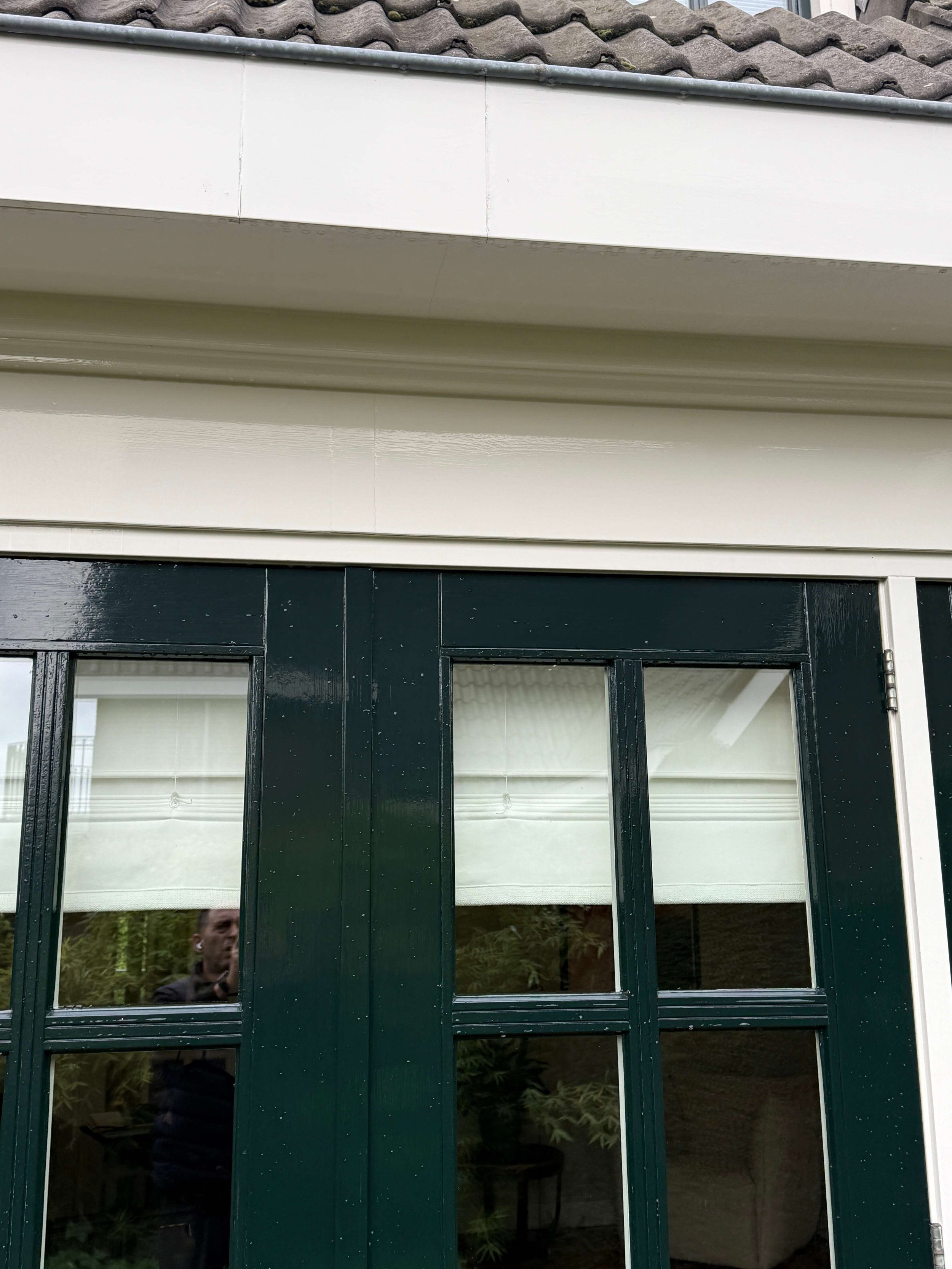 Witte boeidelen boven donkergroene kozijnen aan de buitenzijde van een woning.