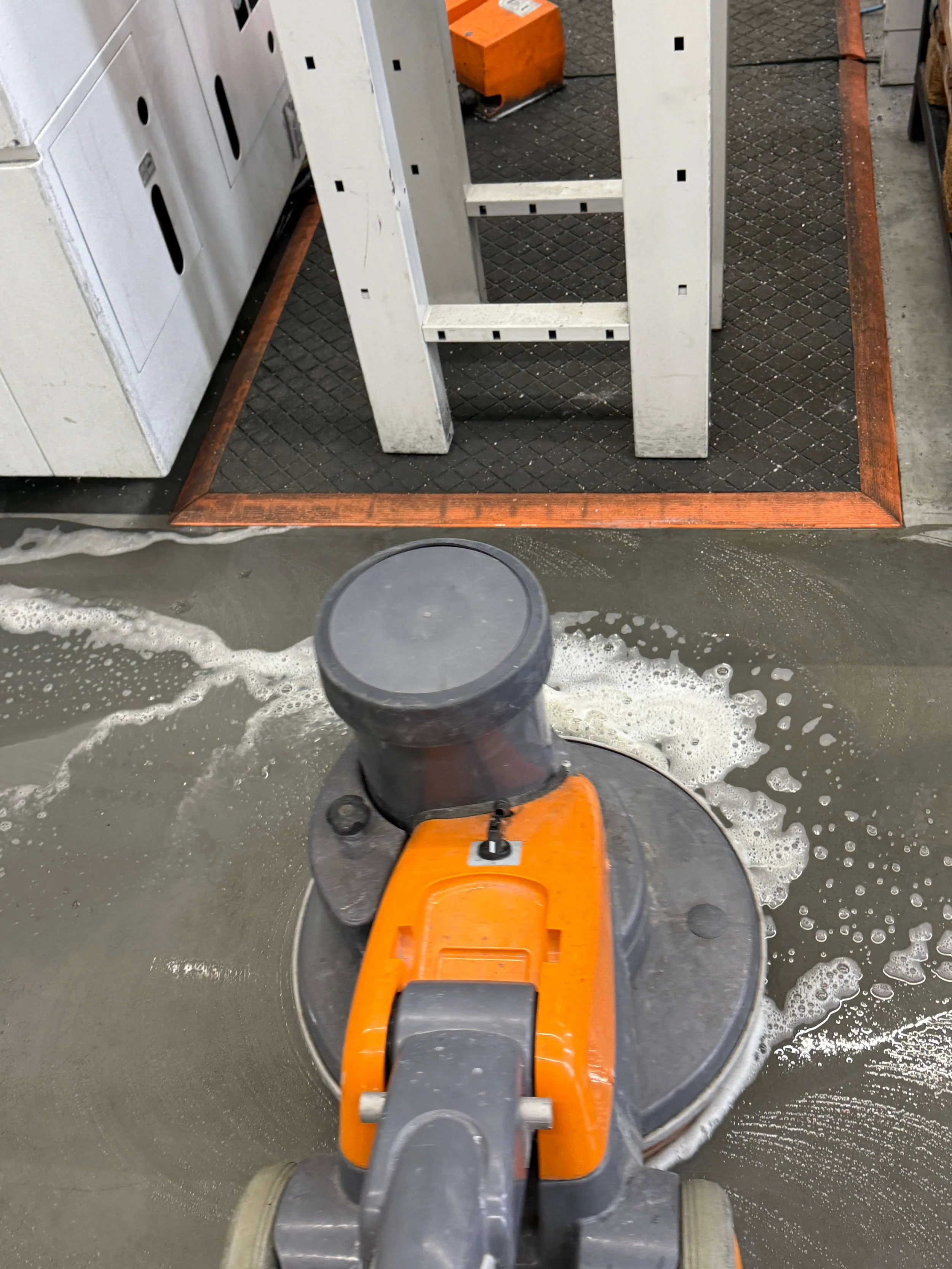 Machinale reiniging van een industriële vloer met een roterende schrobmachine.