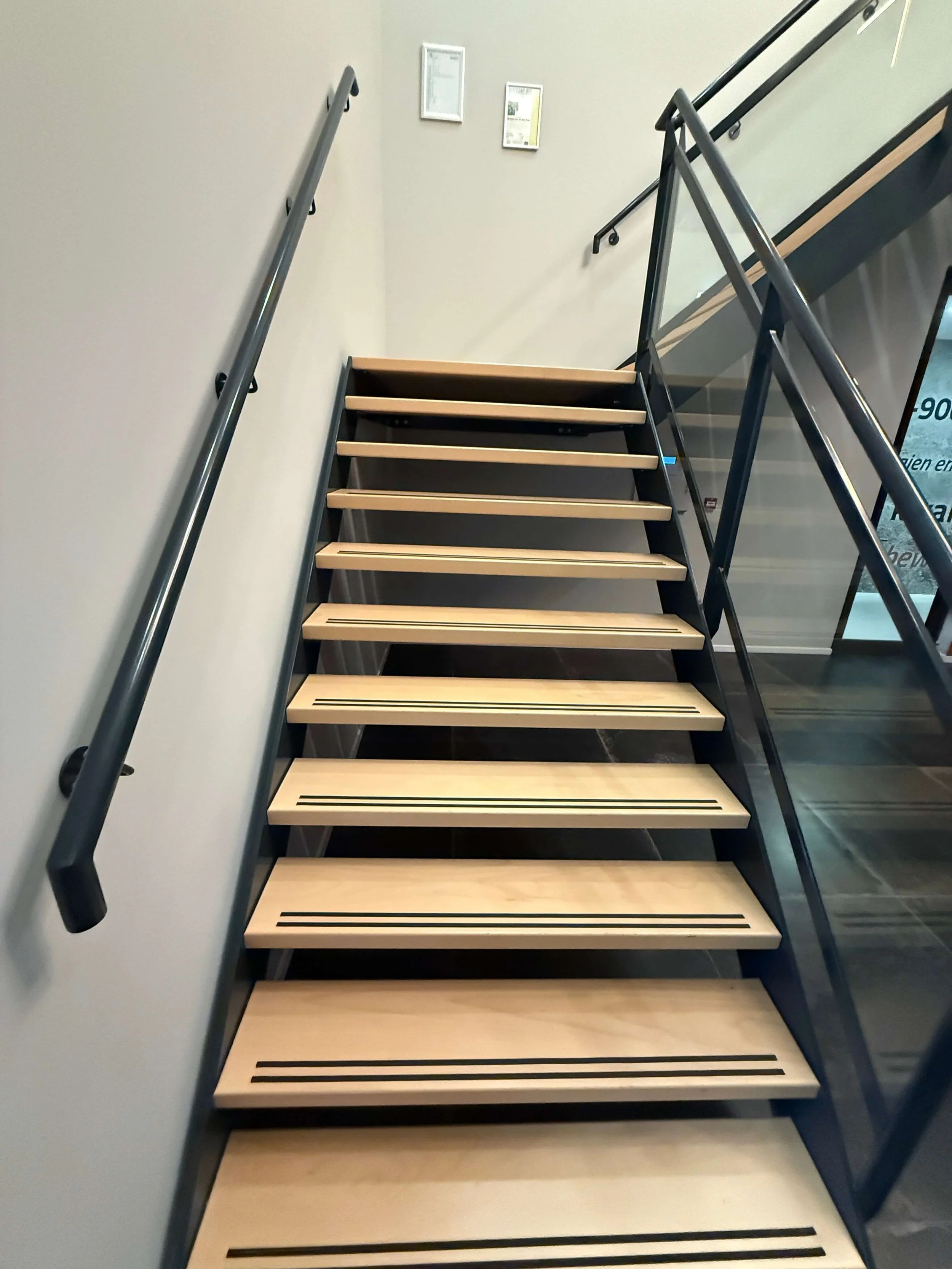 Trappenhuis met houten traptreden, metalen leuningen en glazen balustrade.