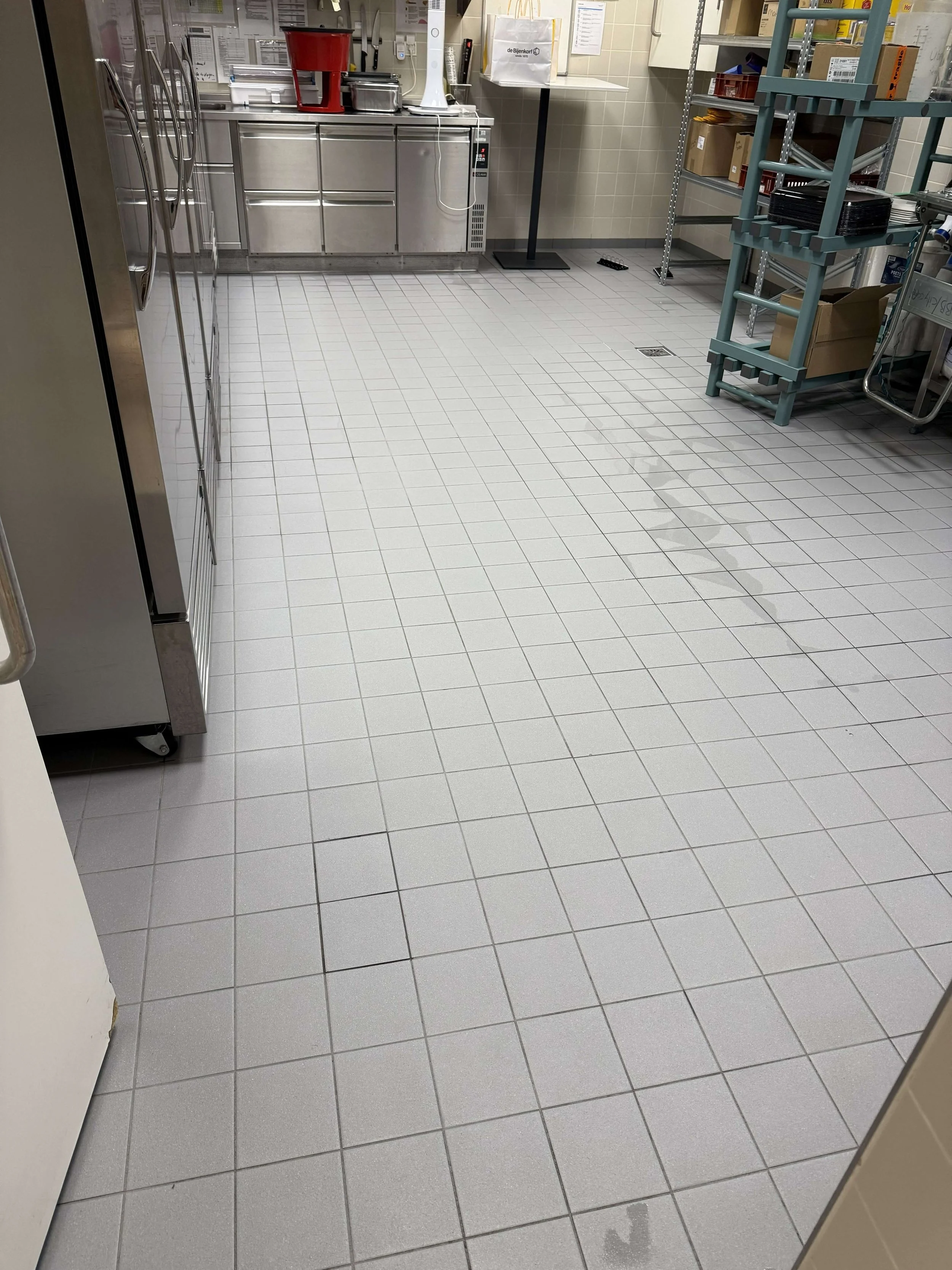 Betegelde vloer en roestvrijstalen werkoppervlakken in een professionele keuken.