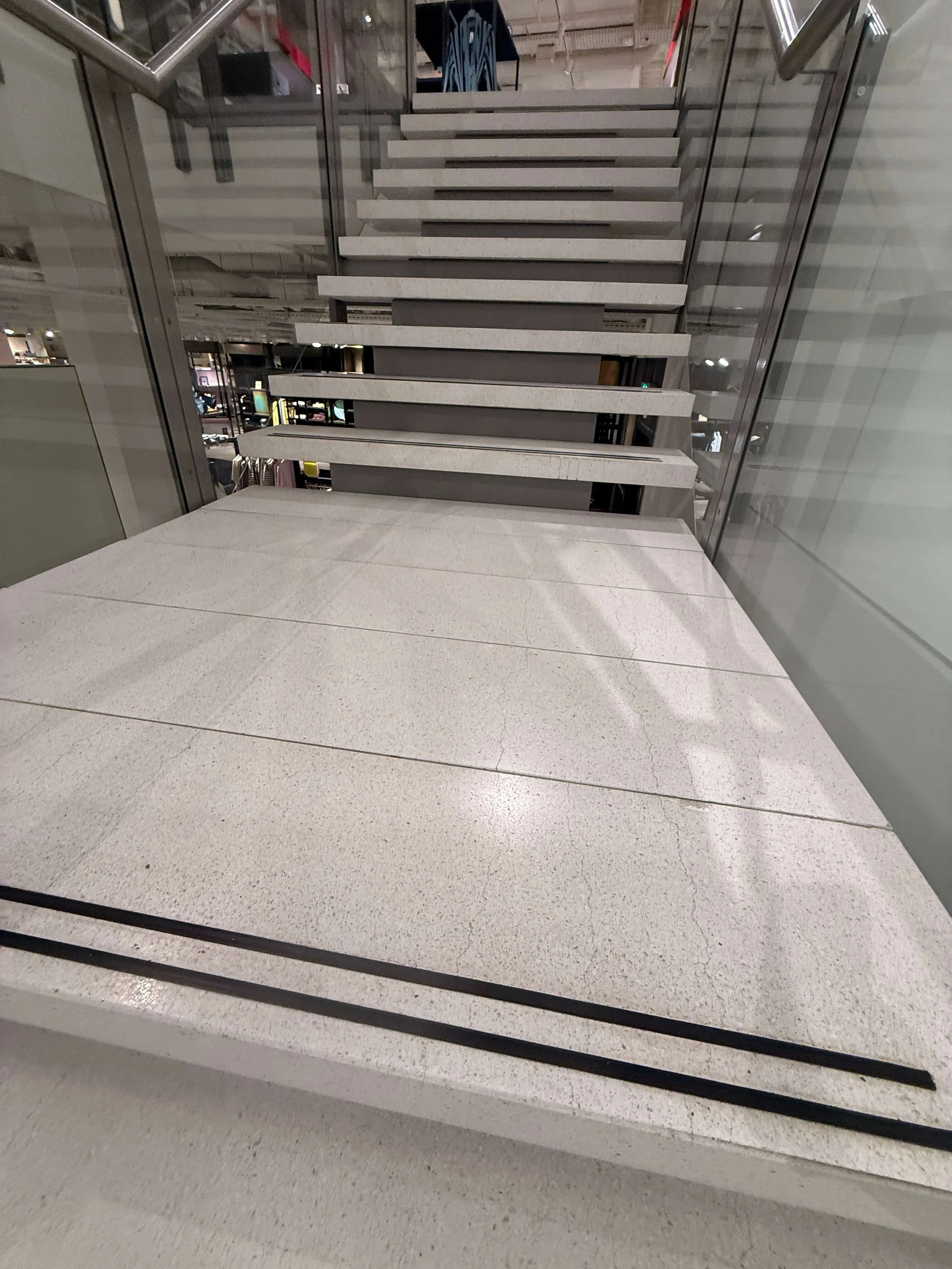 Brede trap met lichte treden en glazen balustrades in een commercieel gebouw.